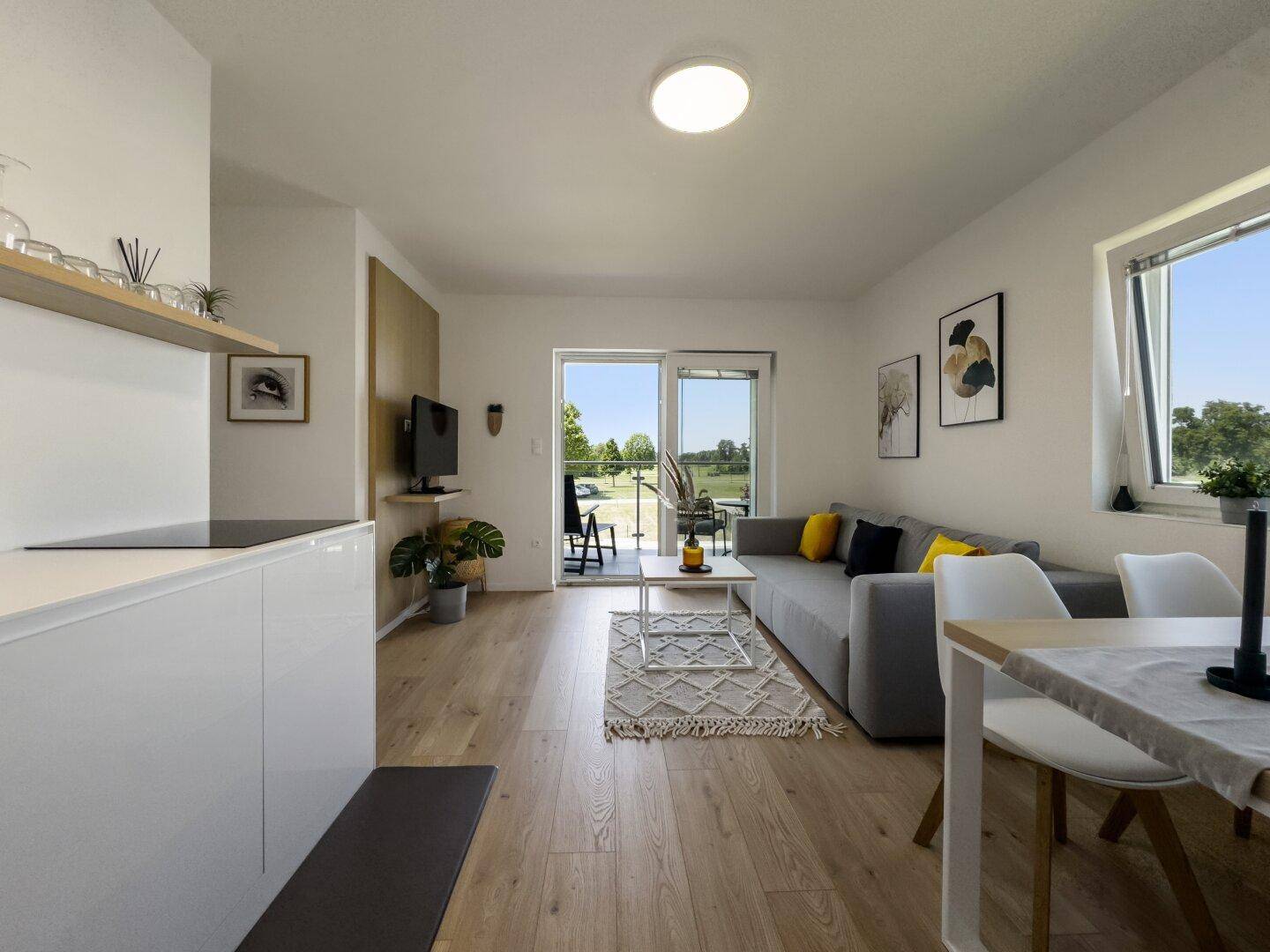 Heller offener Wohn- und Essbereich mit Holzboden und Zugang zum Balkon.