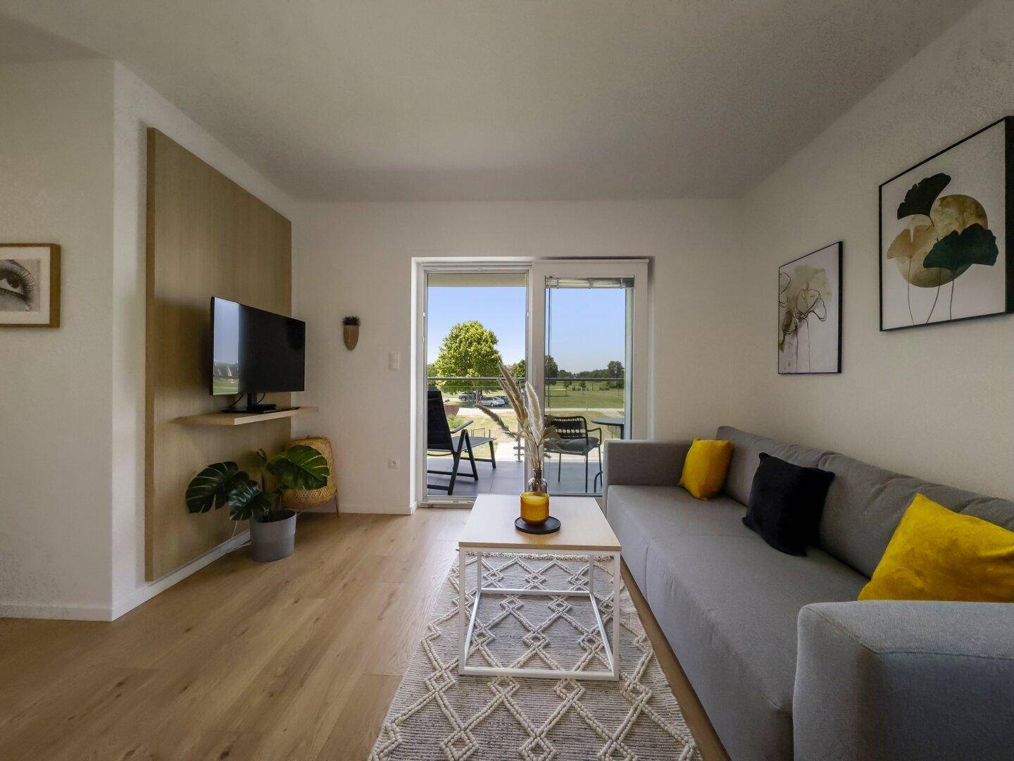 Wohnzimmer mit modernem TV-Bereich, Sofa und direktem Zugang zur Terrasse oder Balkon.