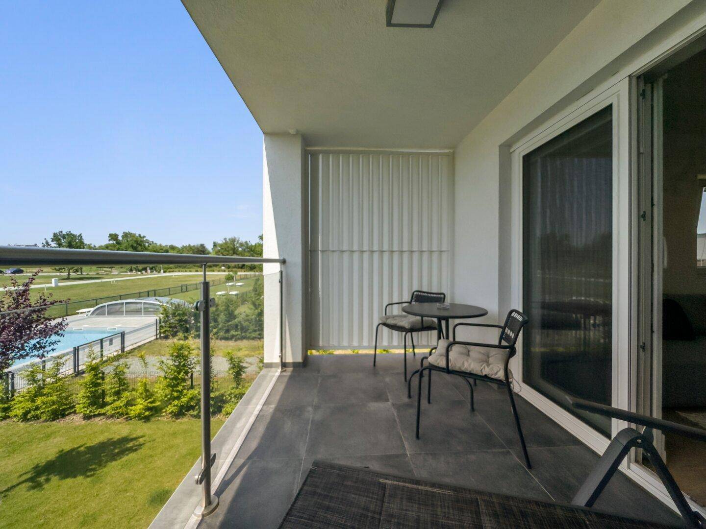 Möblierter Balkon mit Blick auf den Pool und die umliegende Grünfläche.