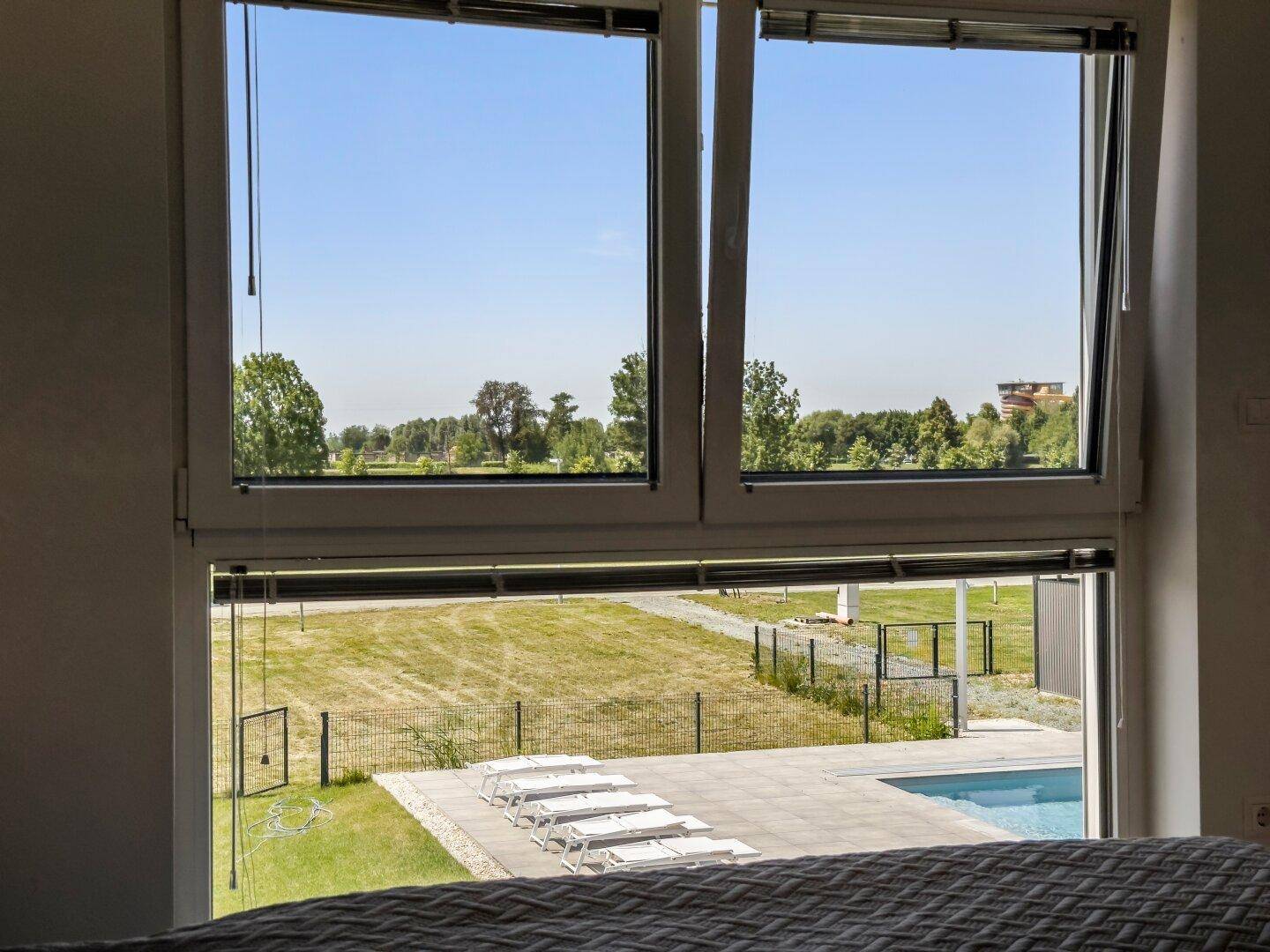 Blick aus dem Schlafzimmerfenster auf den Außenpool und die grüne Landschaft.