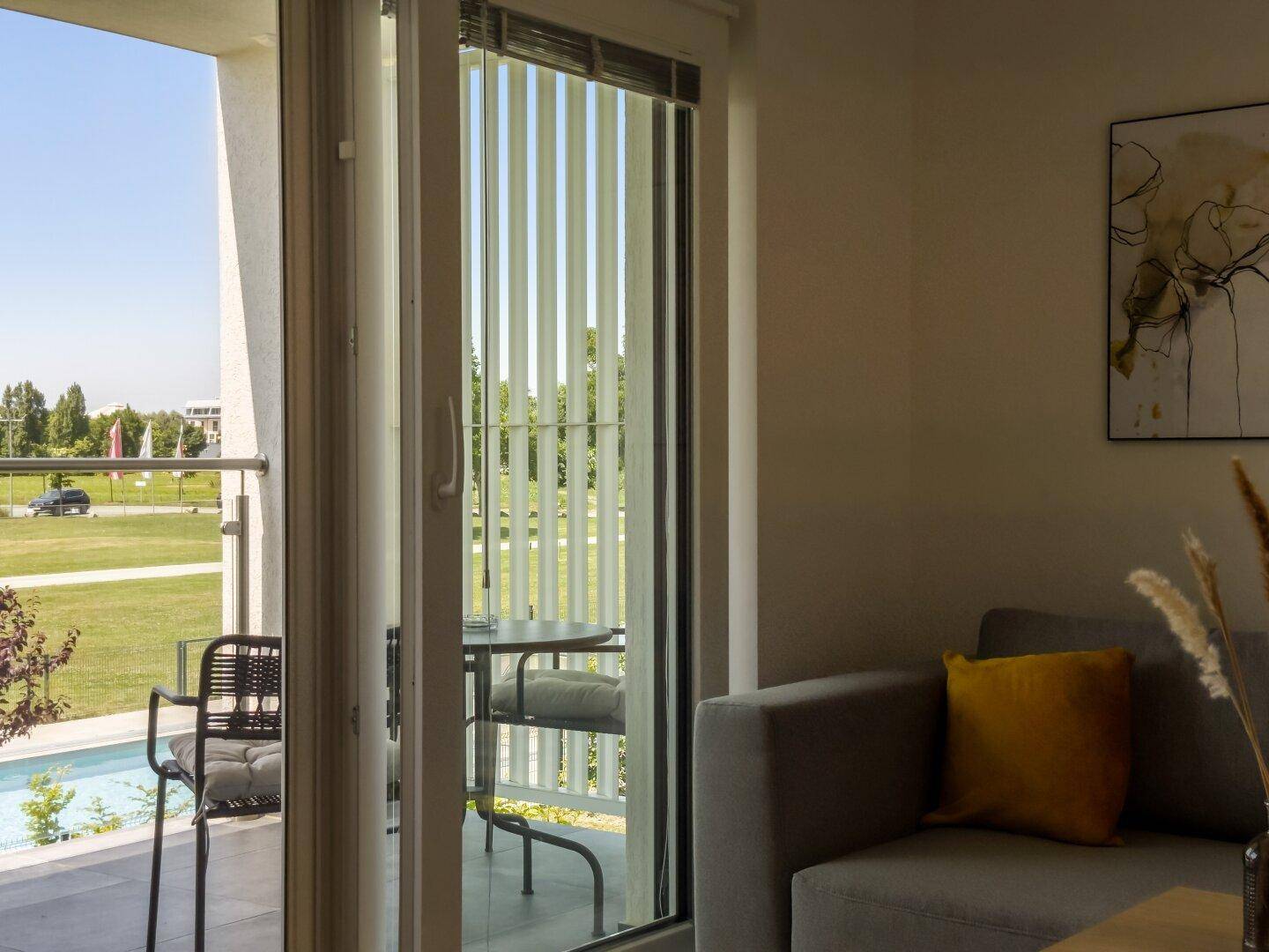 Blick vom Wohnzimmer auf den möblierten Balkon mit Aussicht ins Grüne.
