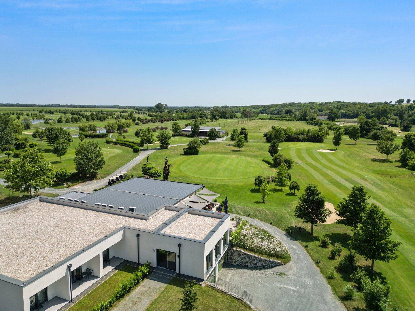 Luftaufnahme eines modernen Gebäudes inmitten einer weitläufigen Golfanlage mit grünen Fairways.