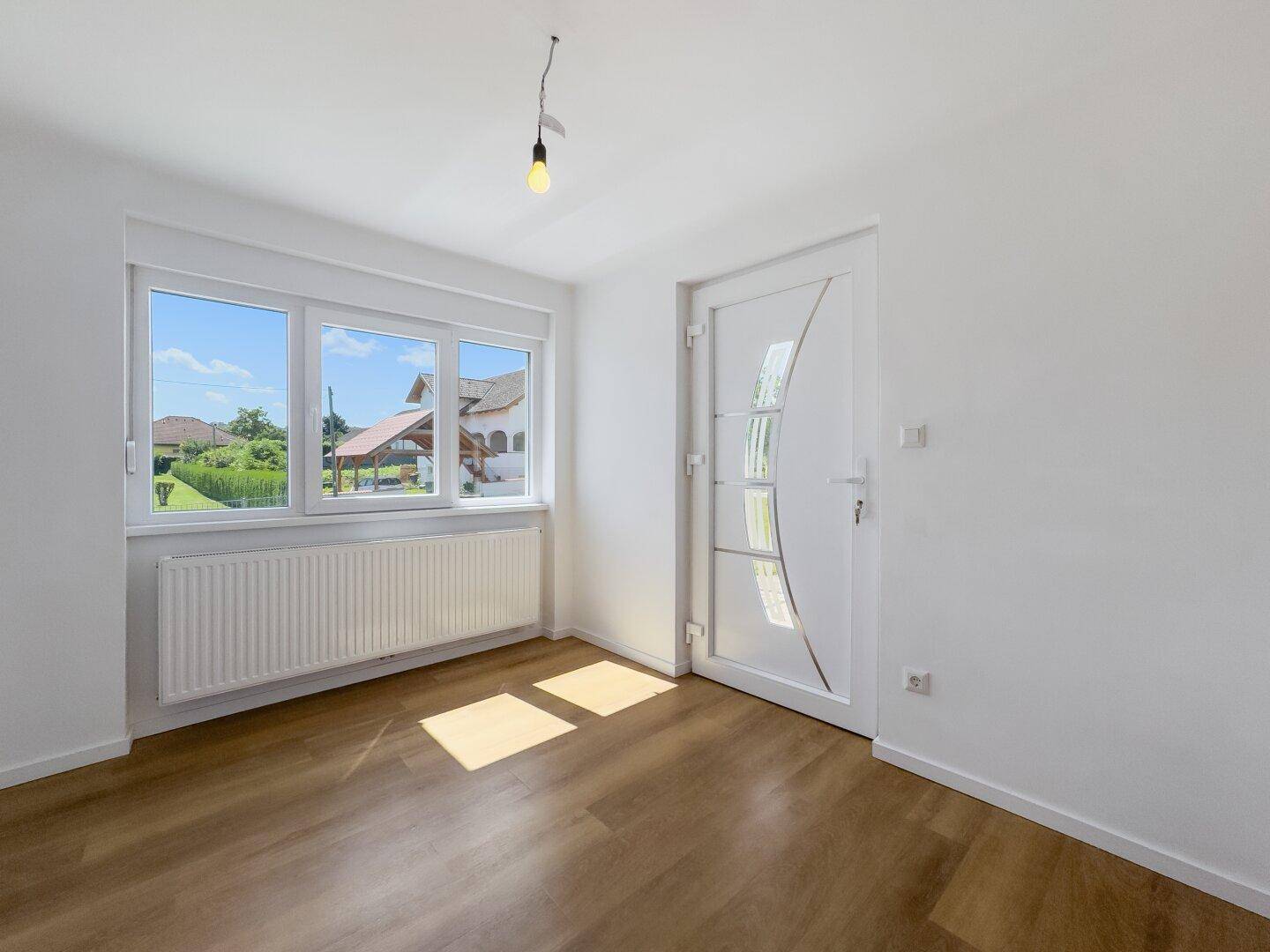 Eingangsbereich mit Laminatboden, heller Tür und Fenster, das viel Licht hereinlässt.