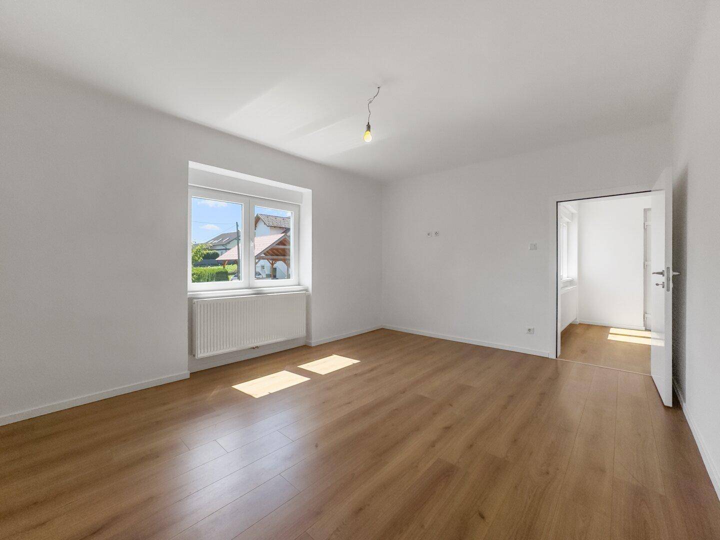 Heller Raum mit Laminatboden und Zugang zu einem weiteren Zimmer, ideal für flexible Nutzung.