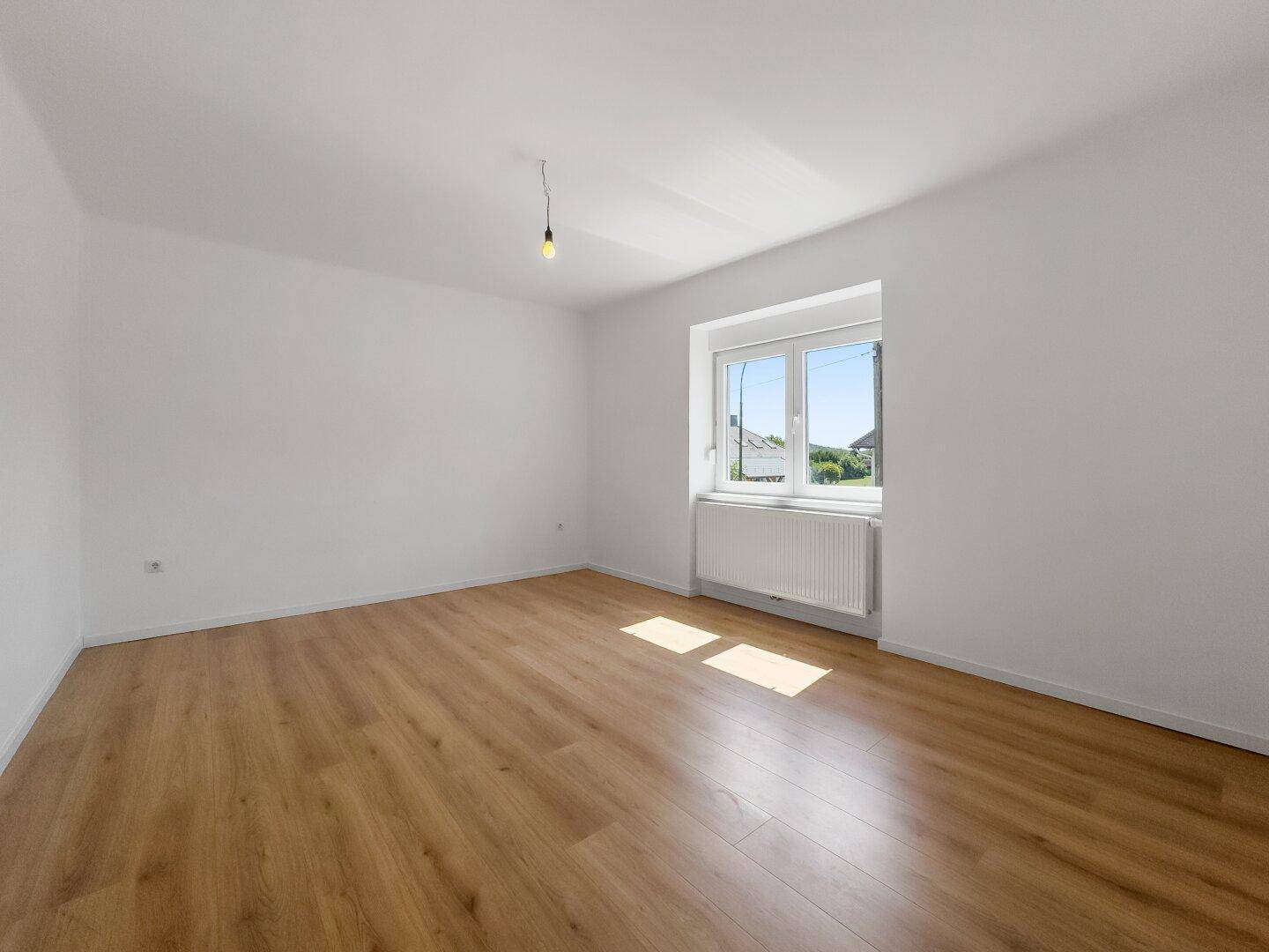 Ruhiges, helles Schlafzimmer mit Laminatboden und Fenster für angenehmes Tageslicht.