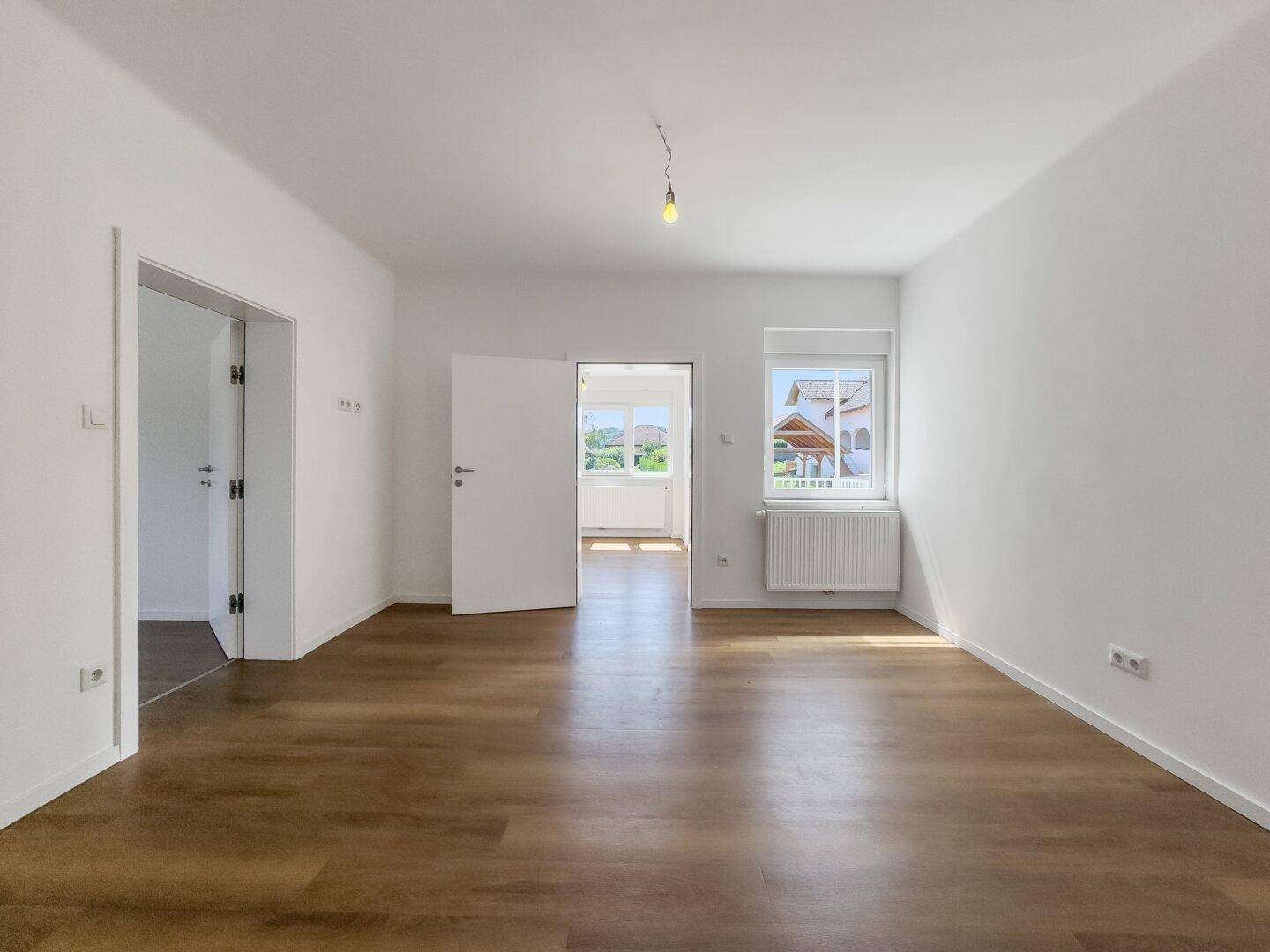 Helles Zimmer mit Laminatboden und Zugang zu weiteren Räumen, ideal als Wohnbereich.
