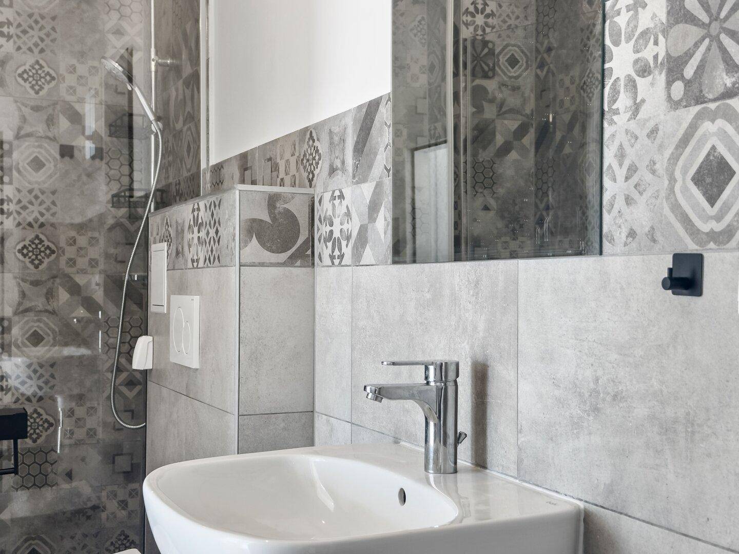 Detailansicht des modernen Badezimmers mit Waschbecken, Spiegel und gemusterten Fliesen.