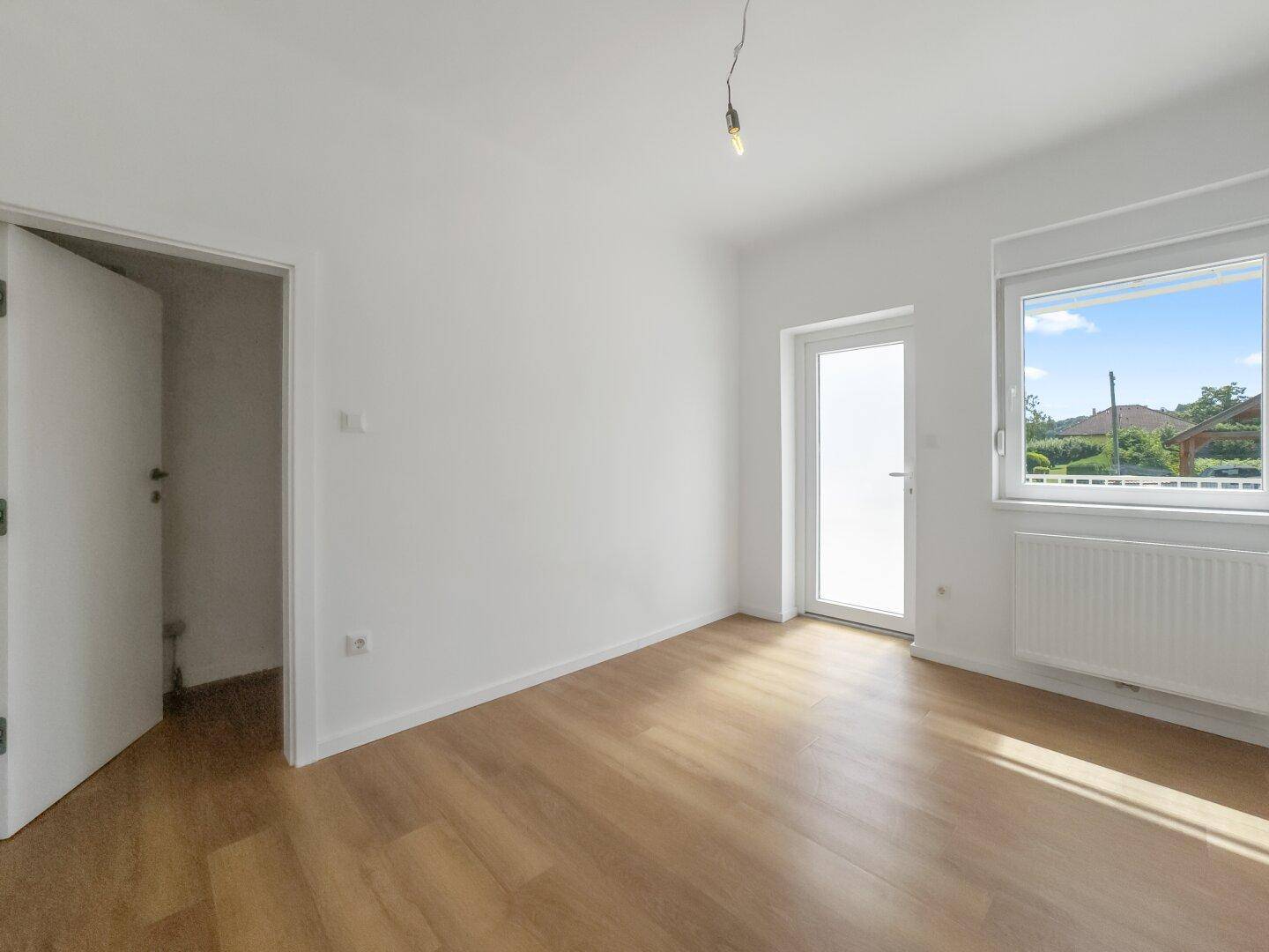 Heller Raum mit Laminatboden und Zugang zu einem Balkon oder einer Terrasse.