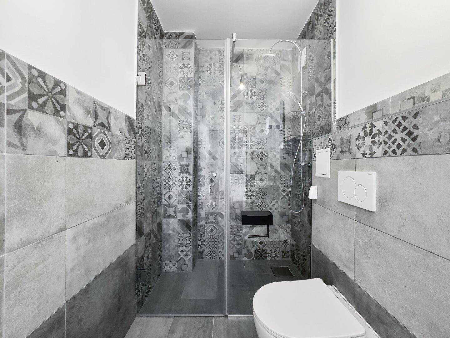 Modernes Badezimmer mit gemusterten Fliesen, ebenerdiger Dusche und wandhängendem WC.