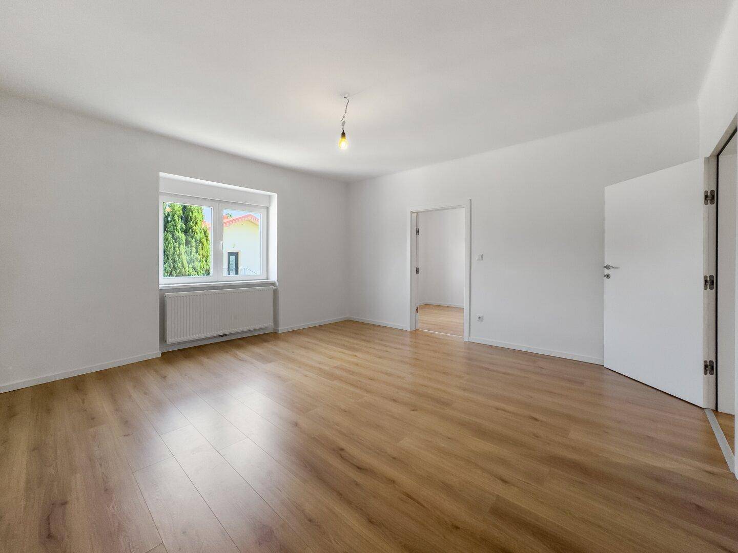 Geräumiges, helles Zimmer mit Laminatboden und Blick ins Grüne durch das Fenster.