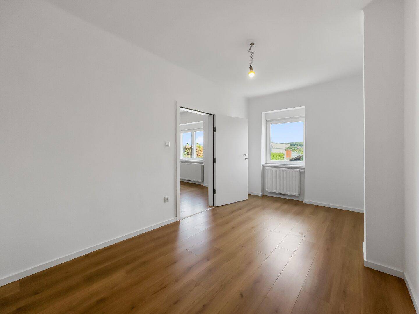 Helles Zimmer mit Laminatboden und Zugang zu einem weiteren Raum, ideal für flexible Gestaltung.