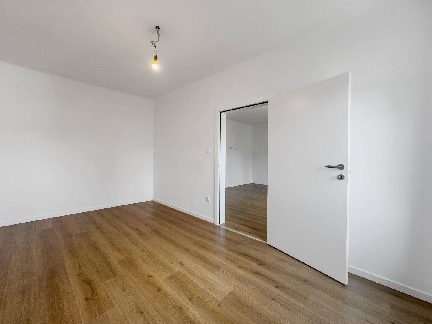 Geräumiges Zimmer mit Laminatboden und Schiebetür zu einem angrenzenden Raum.