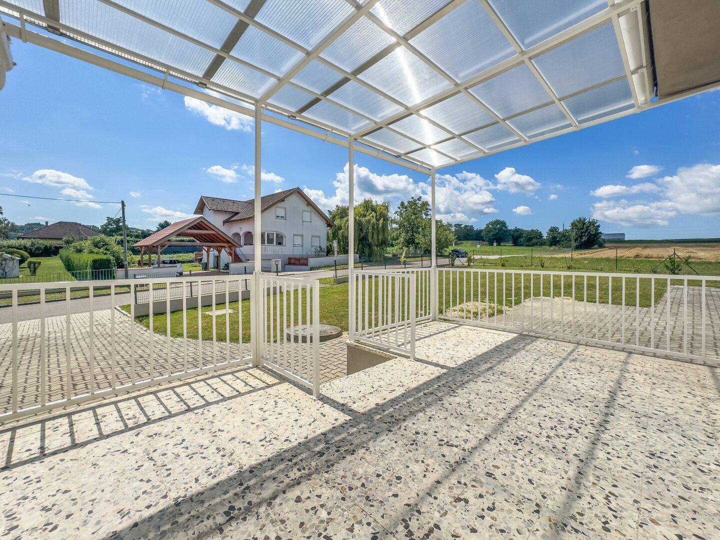 Überdachte Terrasse mit Fliesenboden und Blick auf den Garten und die ländliche Umgebung.
