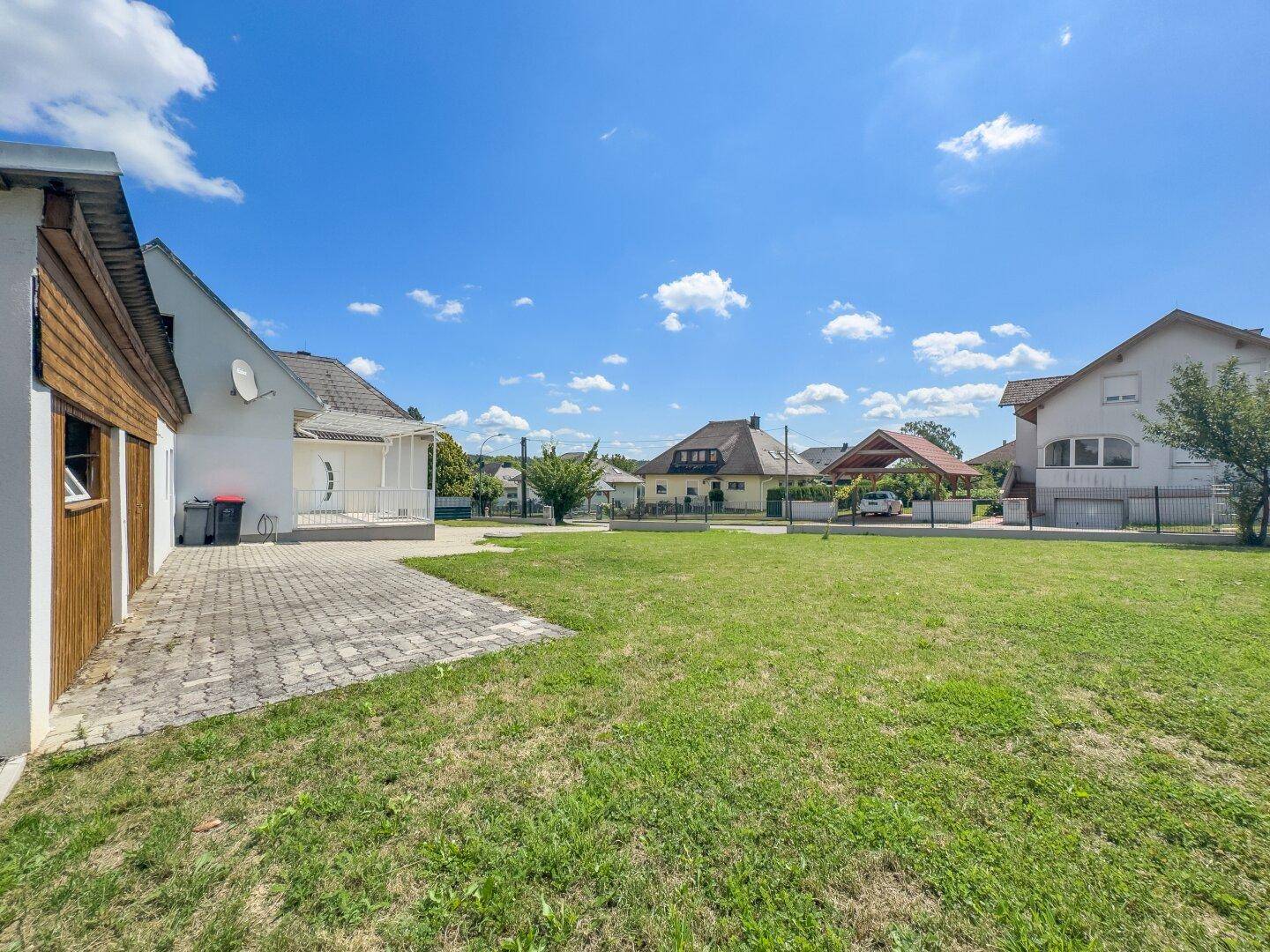 Großer, gepflegter Garten mit Rasenfläche und gepflastertem Bereich neben dem Haus.