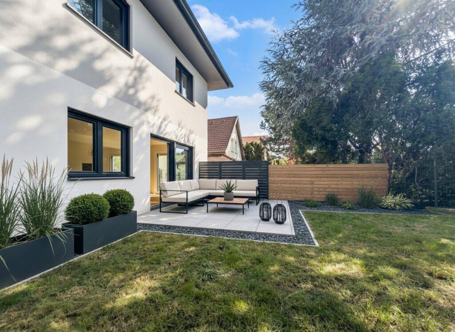 Gepflegter Garten mit moderner Terrasse, Loungemöbeln und dekorativen Pflanzen.