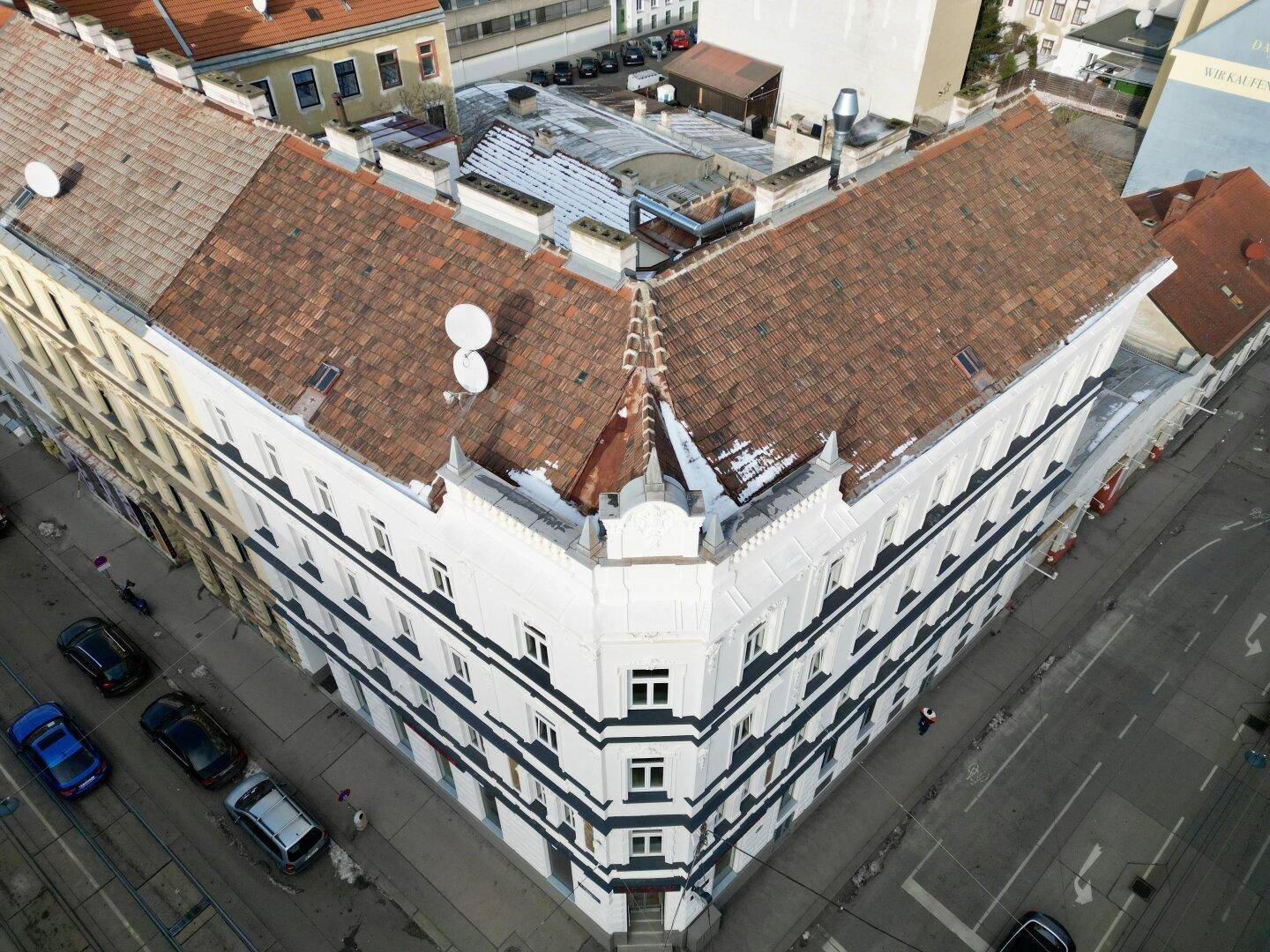 Blick von oben auf ein markantes Eckgebäude mit Ziegeldach und den darunterliegenden Straßenverkehr.