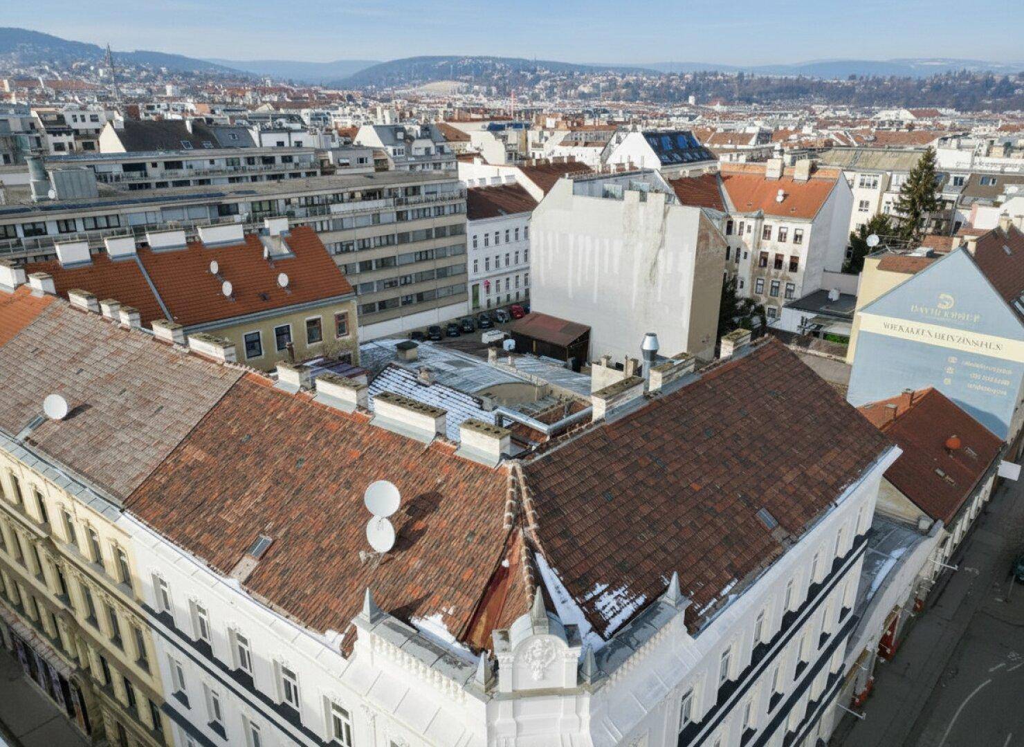 Detaillierte Luftaufnahme eines historischen Eckgebäudes mit Ziegeldach und Blick auf die umliegende Stadt.