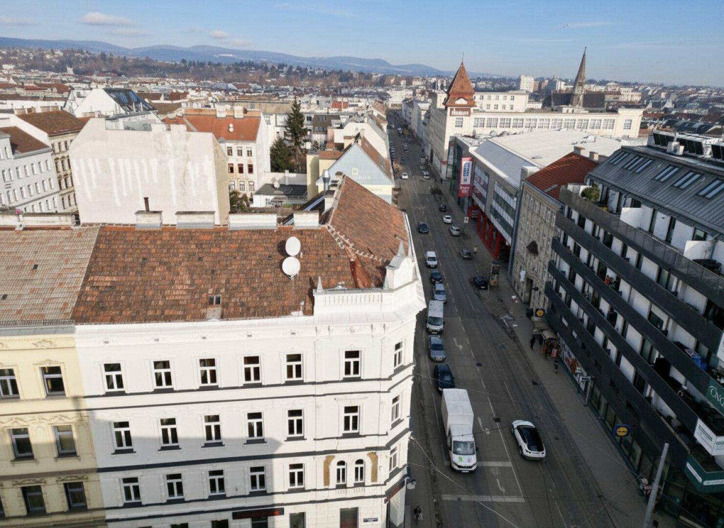 Luftaufnahme einer belebten Stadtstraße mit historischen Gebäuden und einem weiten Blick auf die Umgebung.