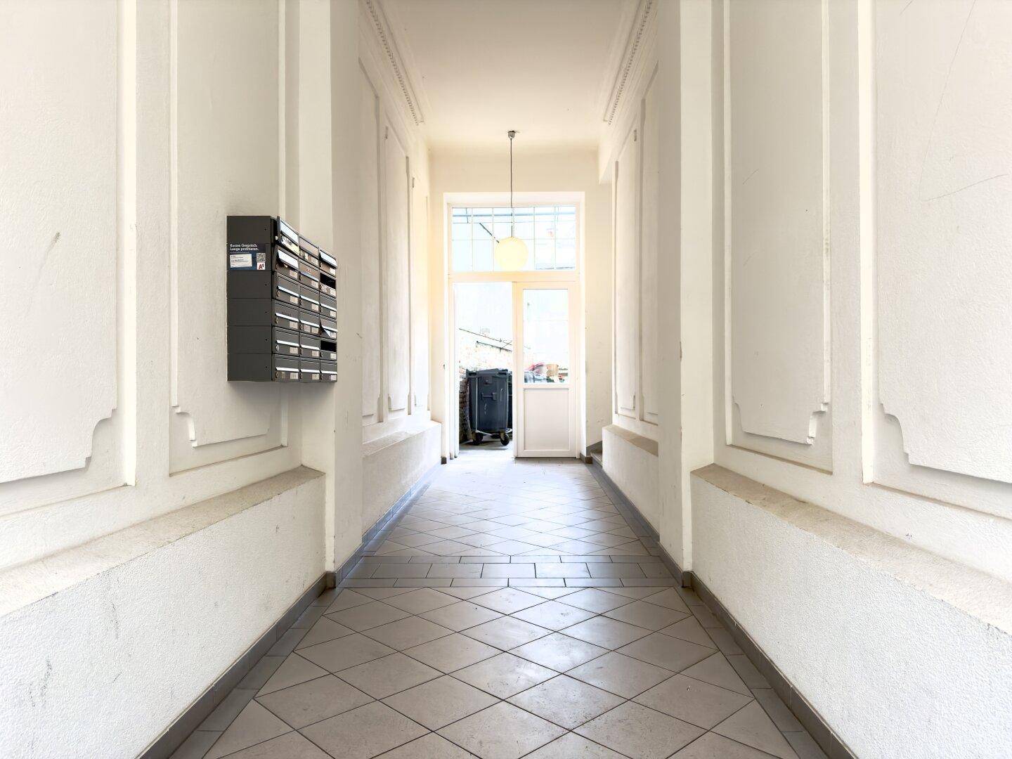 Heller Eingangsbereich mit Fliesenboden, Briefkästen und Zugang zum Innenhof.