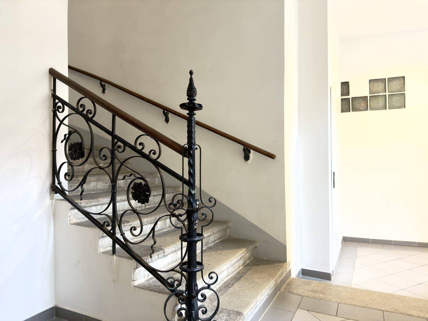 Historisches Treppenhaus mit schmiedeeisernem Geländer und Steinstufen in einem Altbau.
