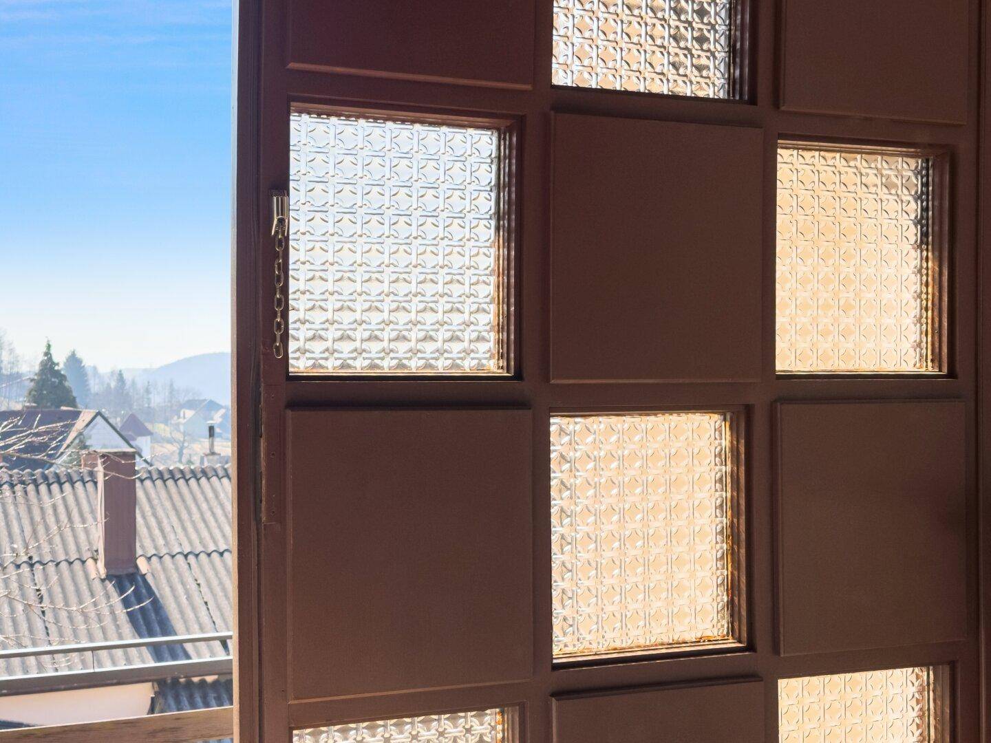 Detailansicht einer Tür mit strukturiertem Glas, die einen Blick nach draußen bietet.