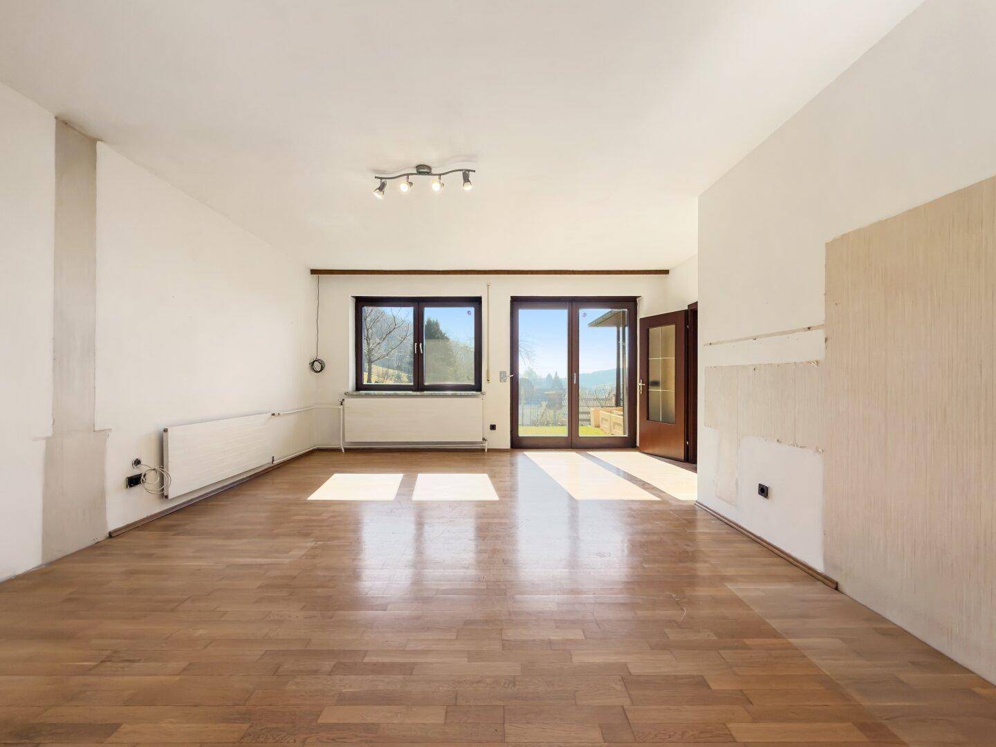 Leerer Raum mit Parkettboden und Zugang zu einem Außenbereich, renovierungsbedürftig.