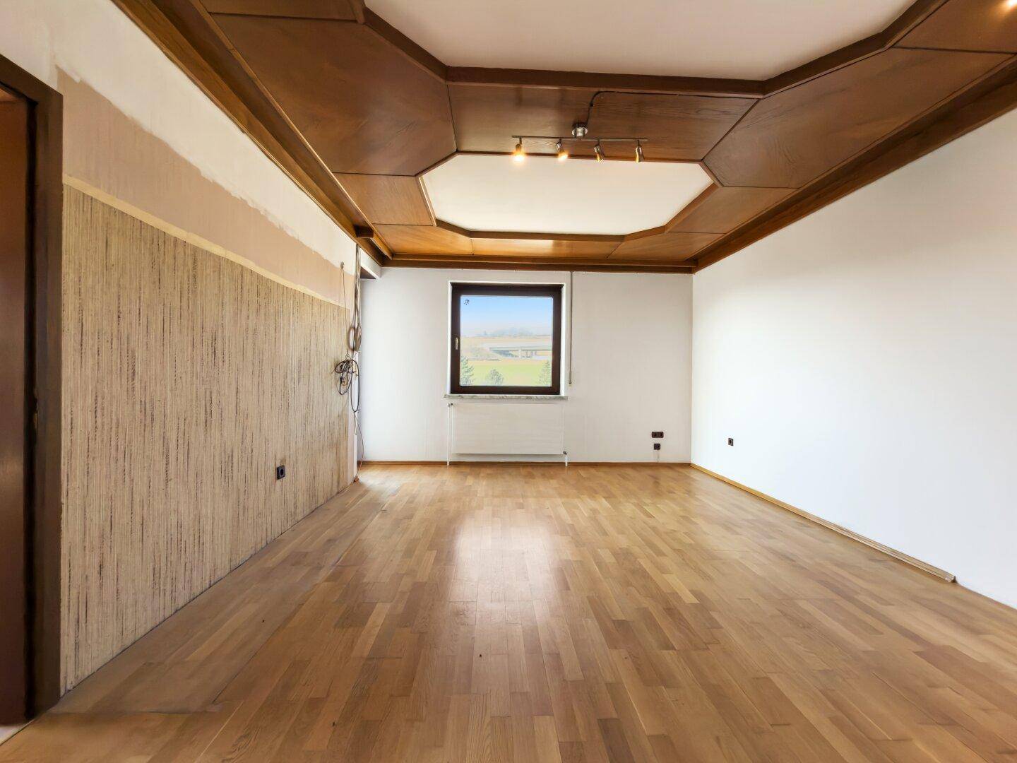 Leeres Wohnzimmer mit Holzbalkendecke und Parkettboden, bereit zur Renovierung.