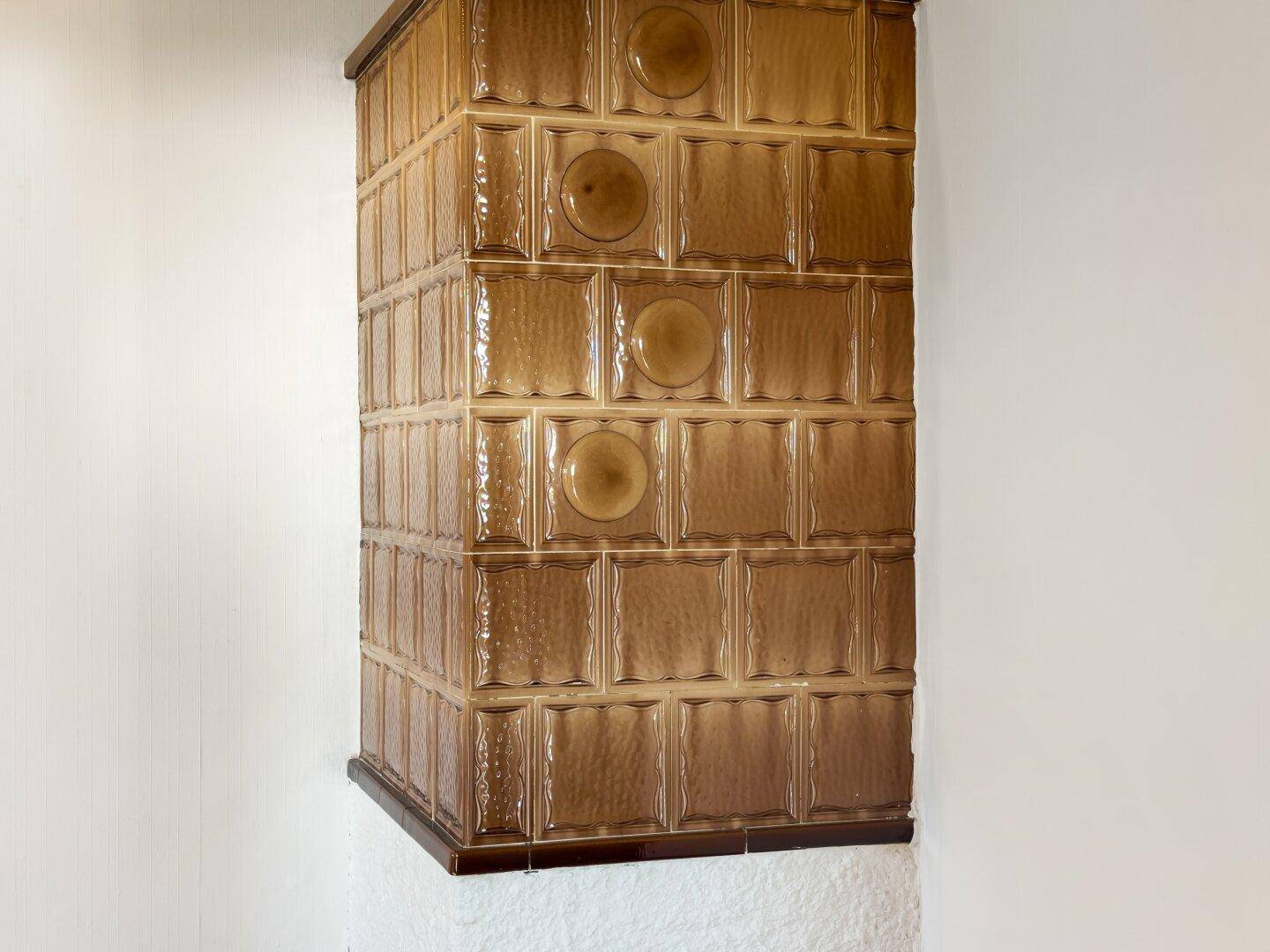 Detailansicht eines traditionellen Kachelofens mit braunen glasierten Fliesen.