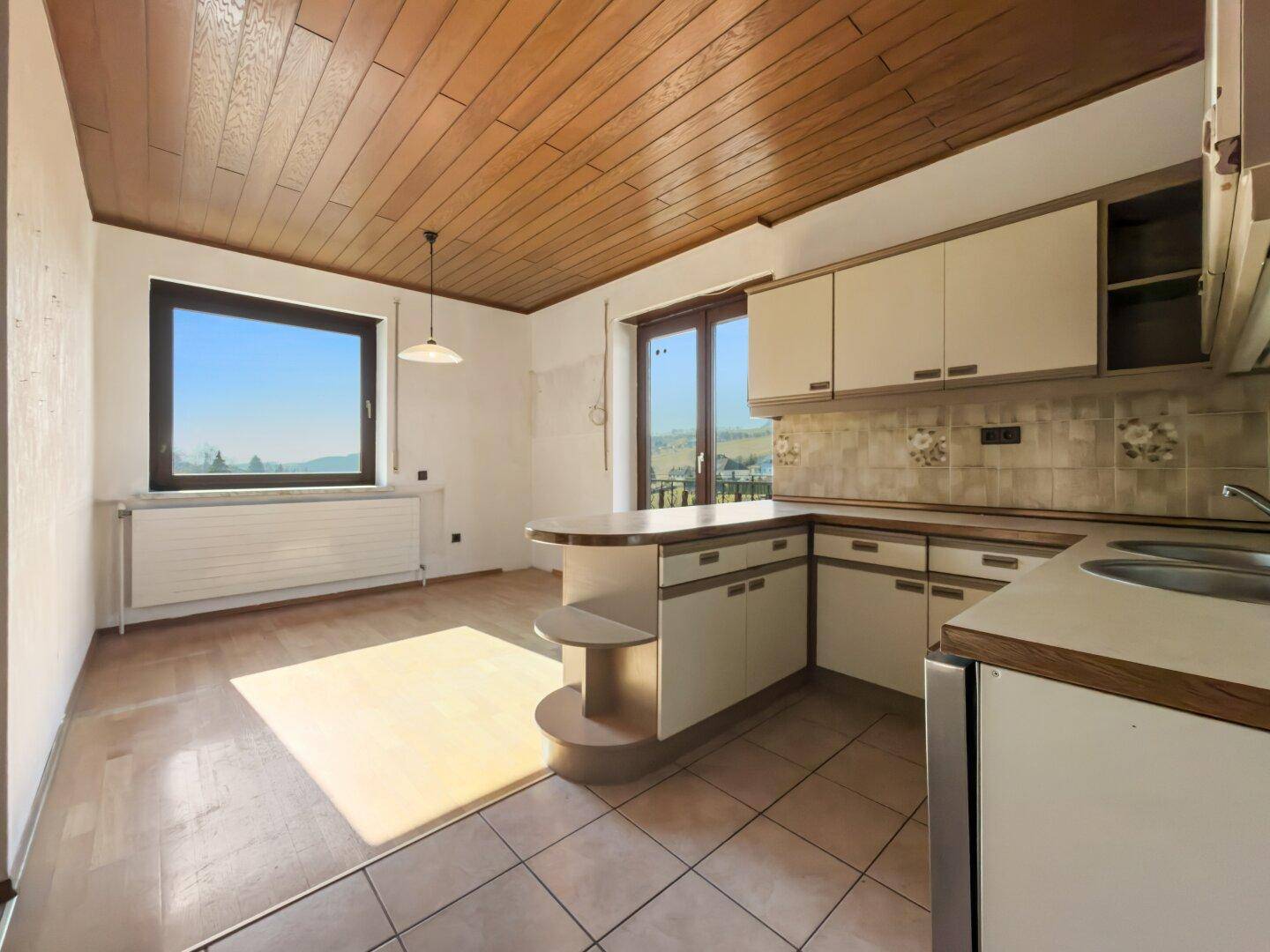 Geräumige Küche mit Holzdecke, Fliesenboden und Zugang zum Balkon.