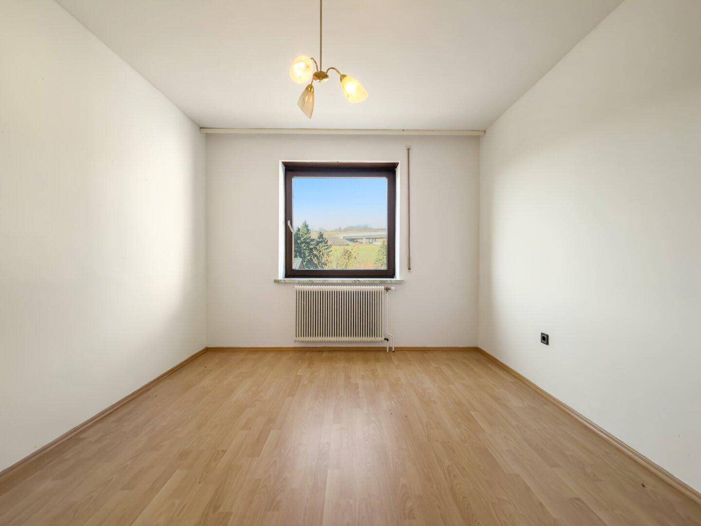 Leerer Raum mit Parkettboden und großem Fenster, ideal für Schlaf- oder Arbeitszimmer.