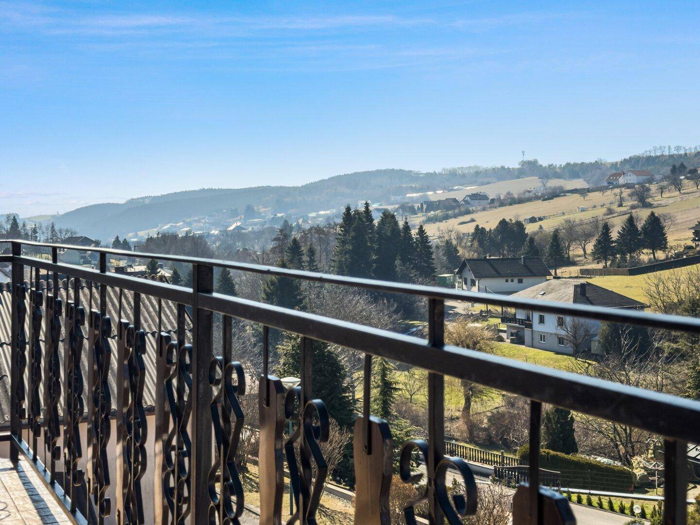 Panoramablick vom Balkon über die hügelige, grüne Landschaft und umliegende Häuser.