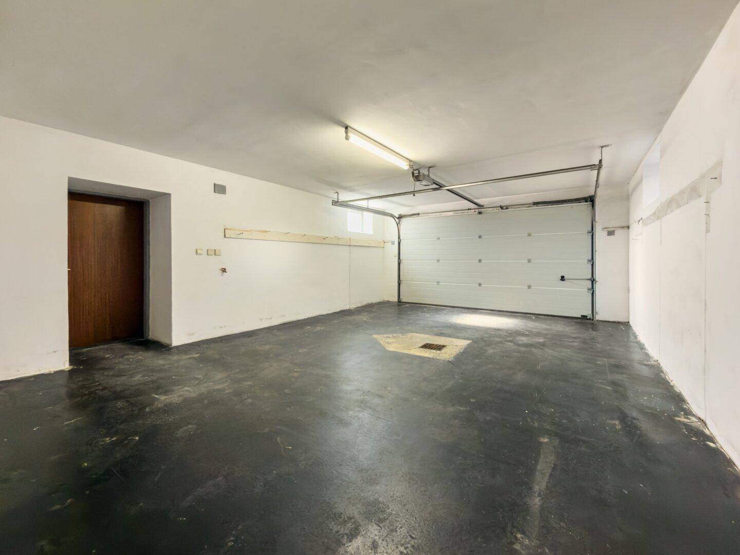 Geräumige Garage mit Rolltor und Betonboden, bietet Platz für mehrere Fahrzeuge.