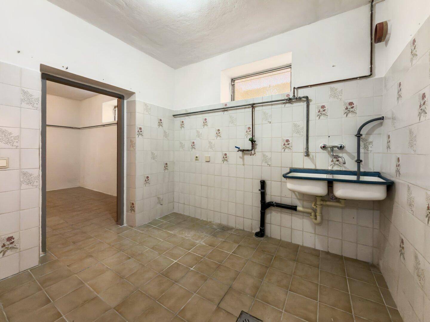 Hauswirtschaftsraum mit Fliesenboden, Waschbecken und Anschlussmöglichkeiten.