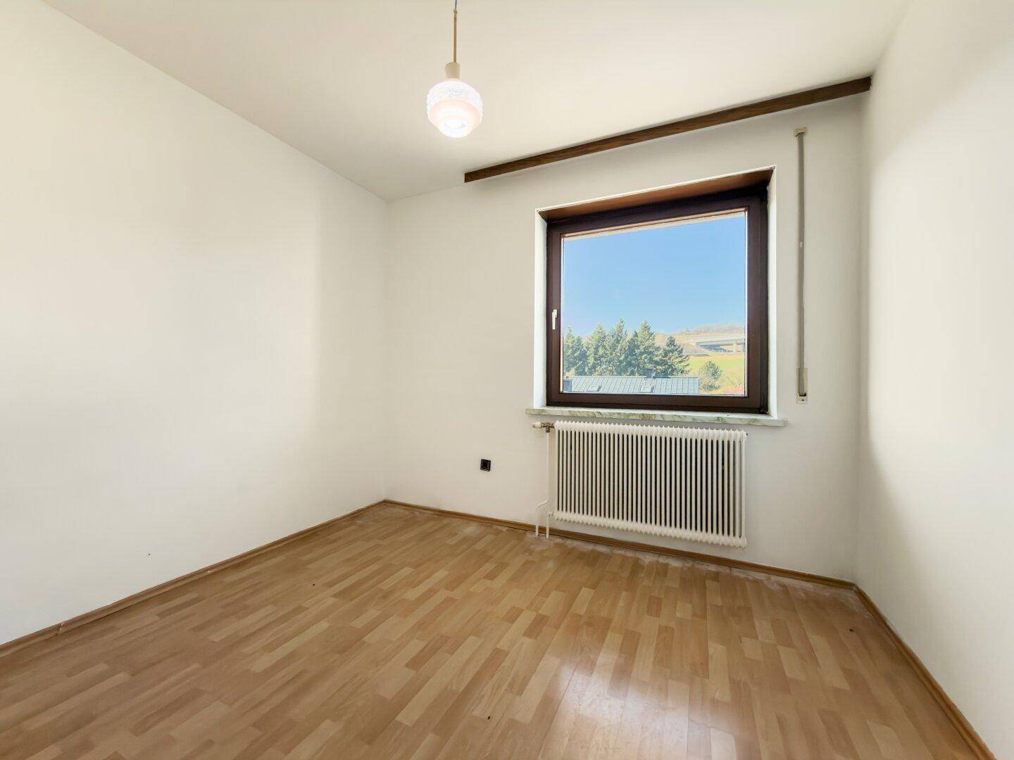 Leeres Schlafzimmer mit Parkettboden und großem Fenster, bereit zur Renovierung.