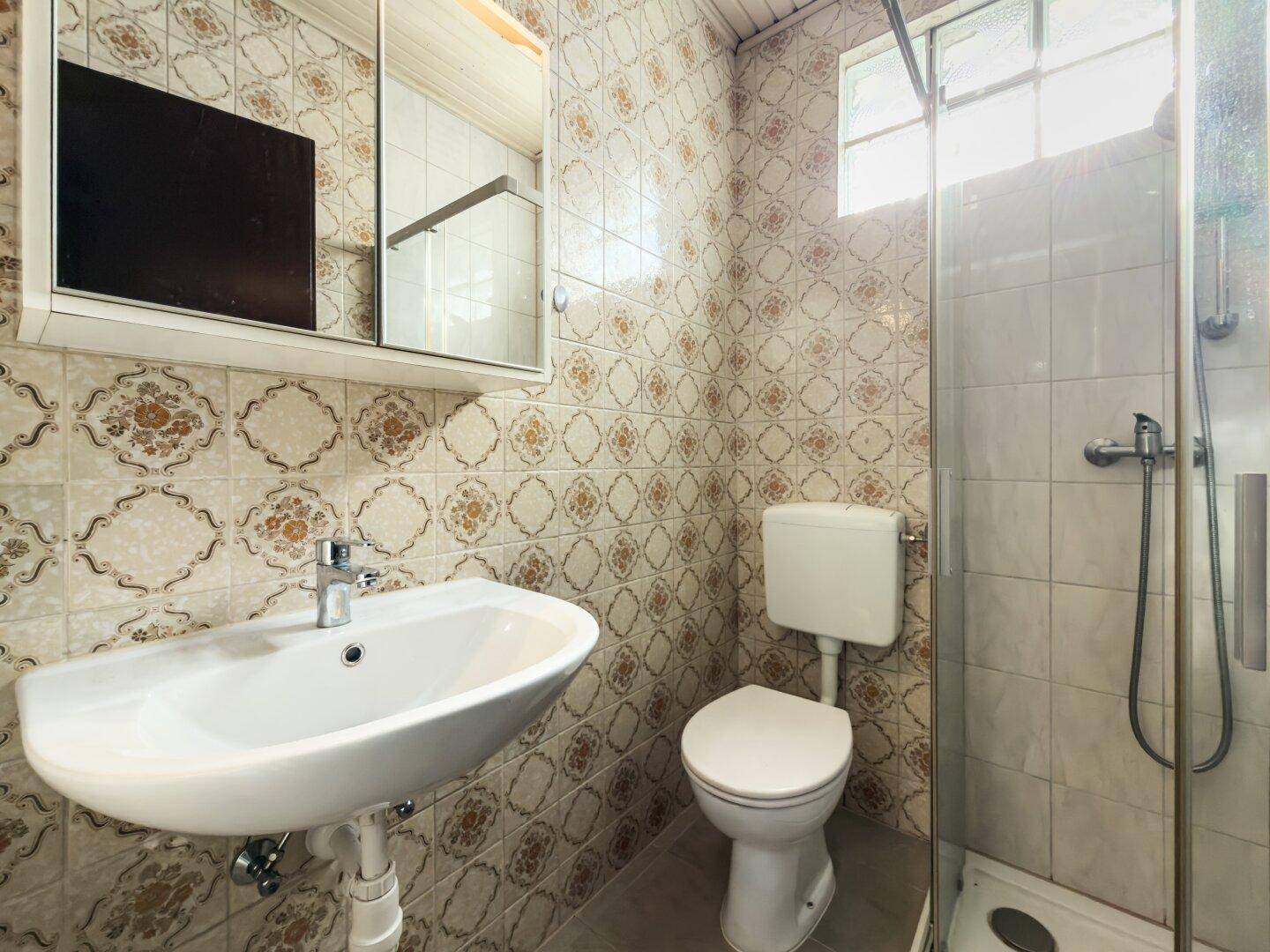 Kleines Badezimmer mit Duschkabine, Waschbecken und WC, im älteren Stil.