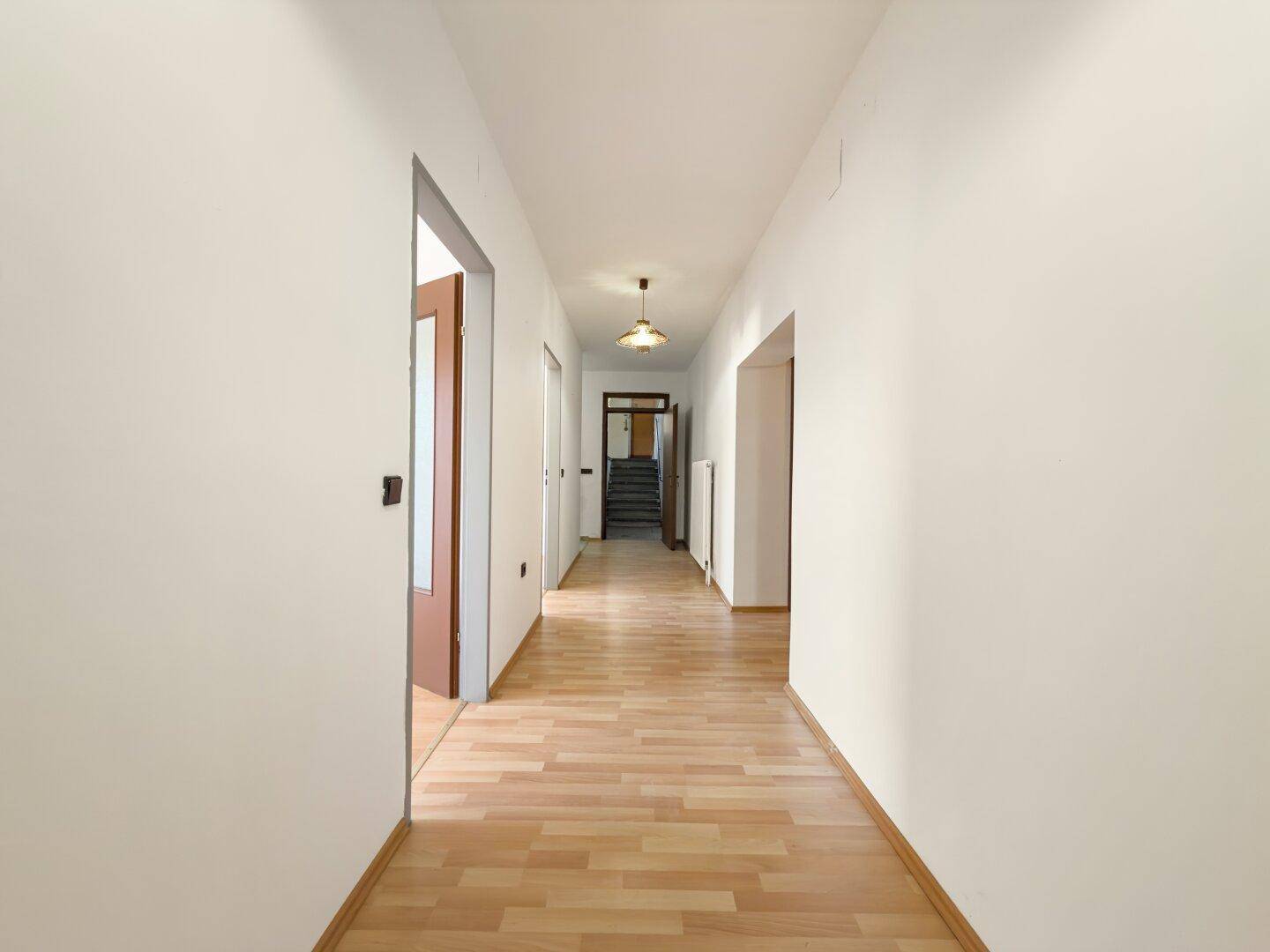 Langer Flur mit Laminatboden und weißen Wänden, der zu mehreren Räumen führt.