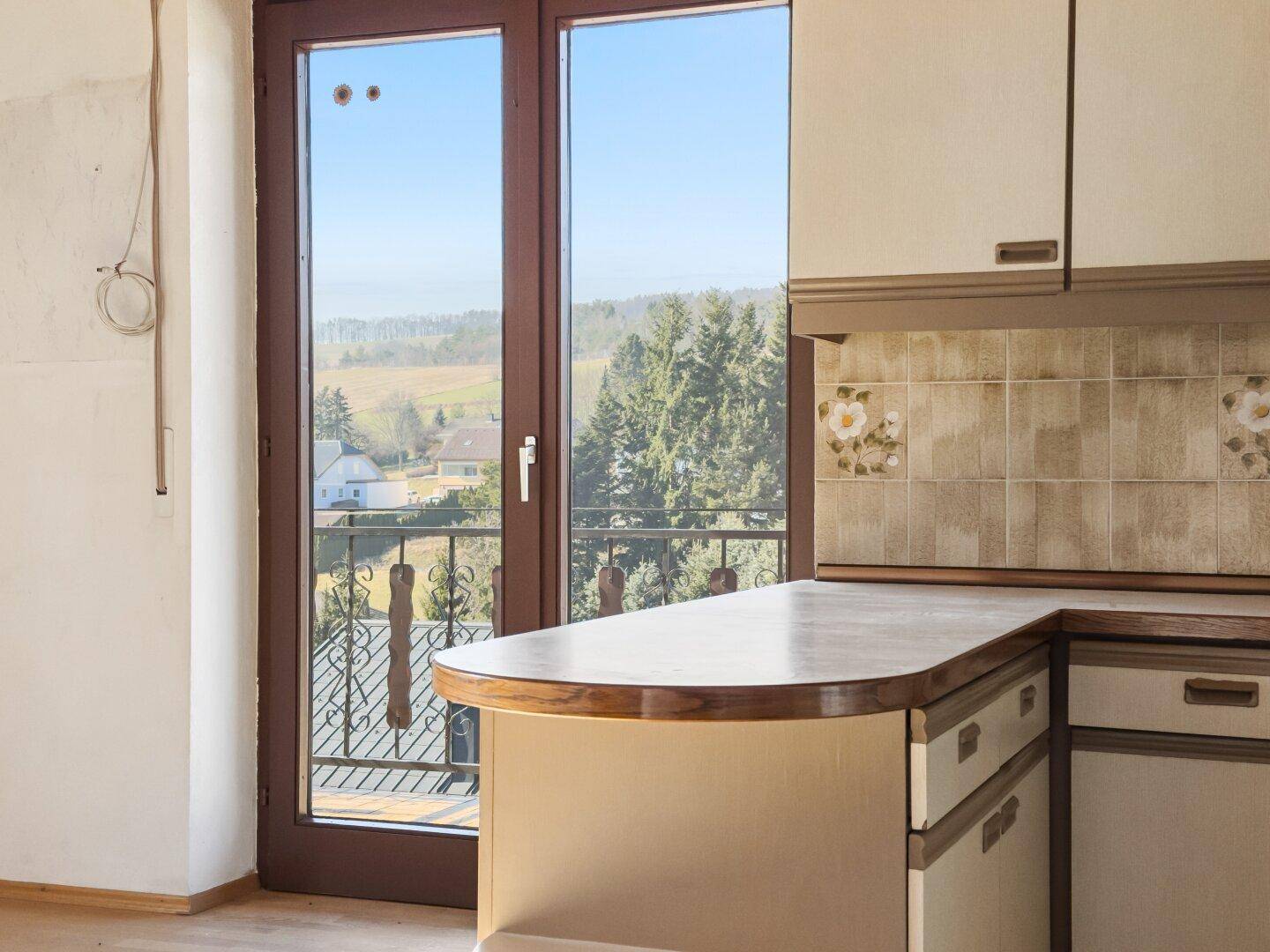 Ältere Küche mit Balkonzugang und Blick auf die grüne Umgebung.