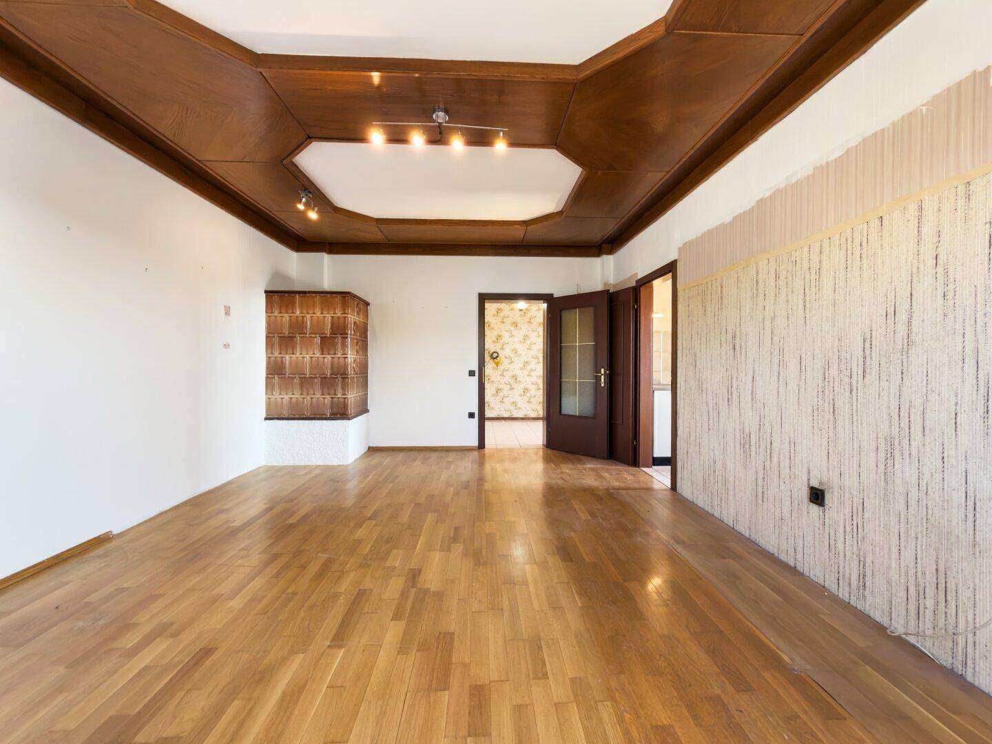 Leerer Essbereich mit Holzbalkendecke, Parkettboden und Kachelofen.