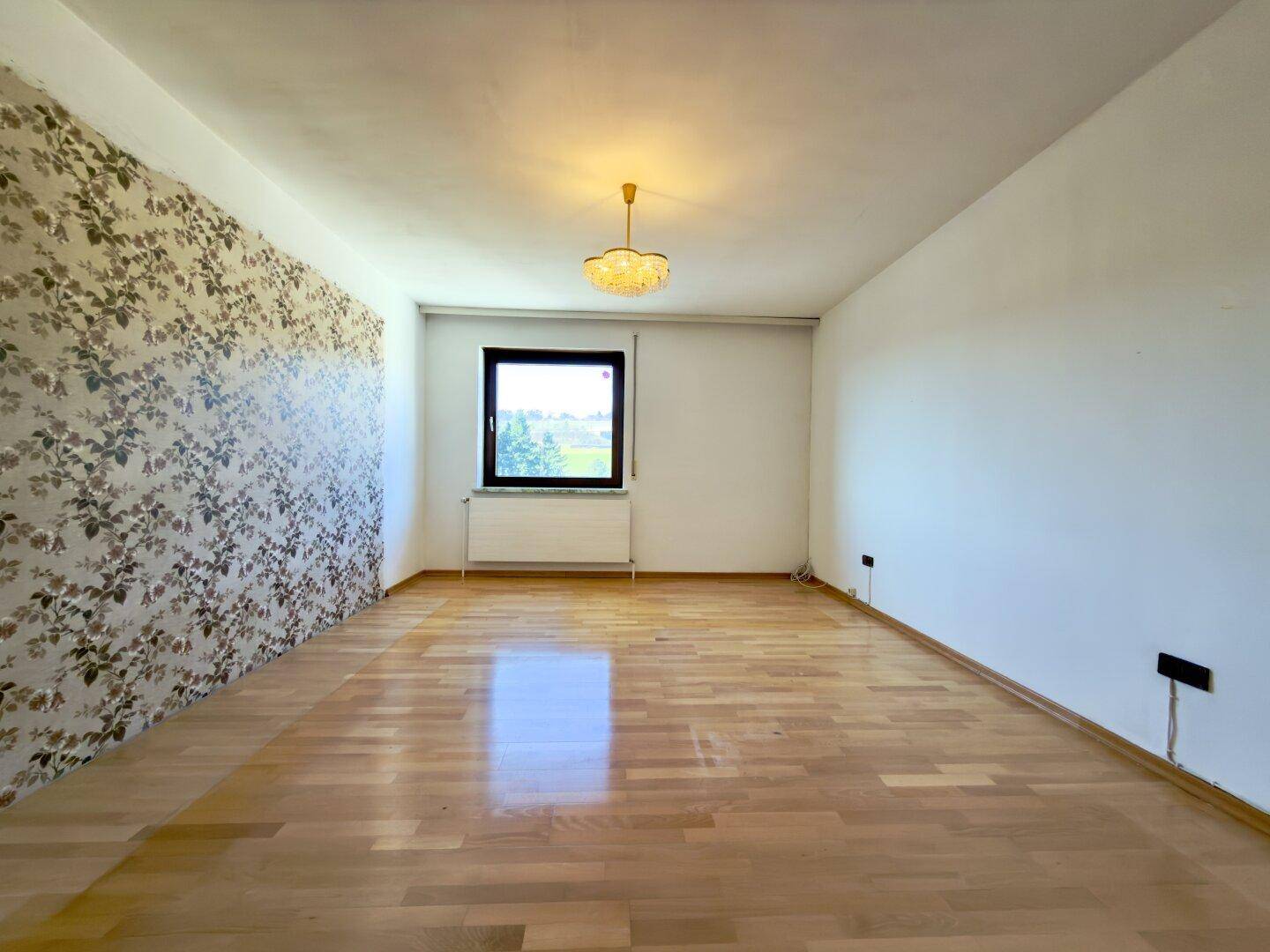 Leeres Schlafzimmer mit Parkettboden und floraler Tapete, bereit zur Neugestaltung.