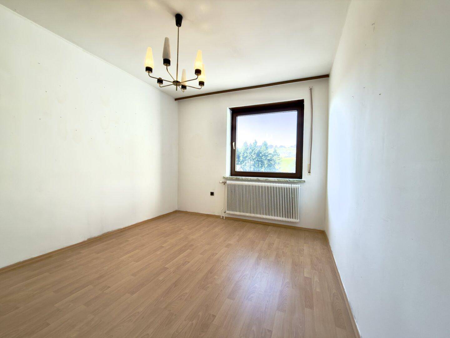 Leerer Raum mit Parkettboden und großem Fenster, bereit zur individuellen Gestaltung.