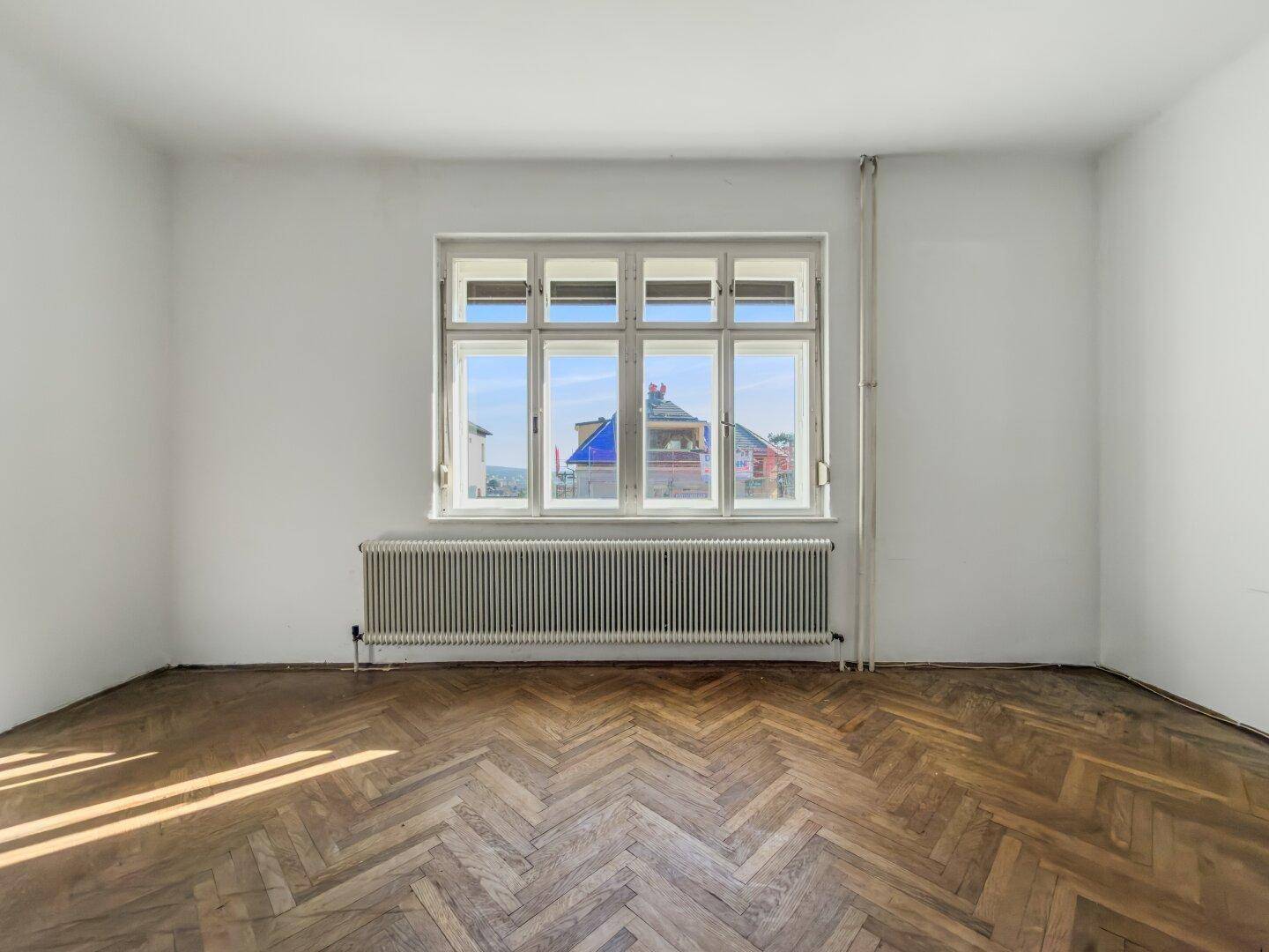 Helles, unmöbliertes Zimmer mit Fischgrätparkett und großem Fenster, ideal für individuelle Gestaltung.