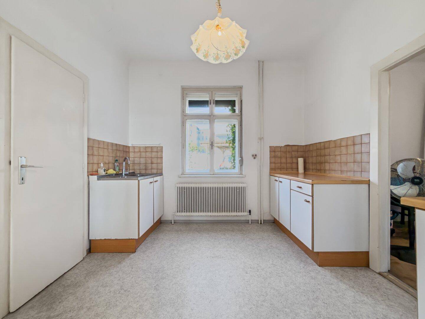 Unmöblierte Küche mit weißen Unterschränken, Holztheke und Fliesenboden, bereit zur Renovierung.