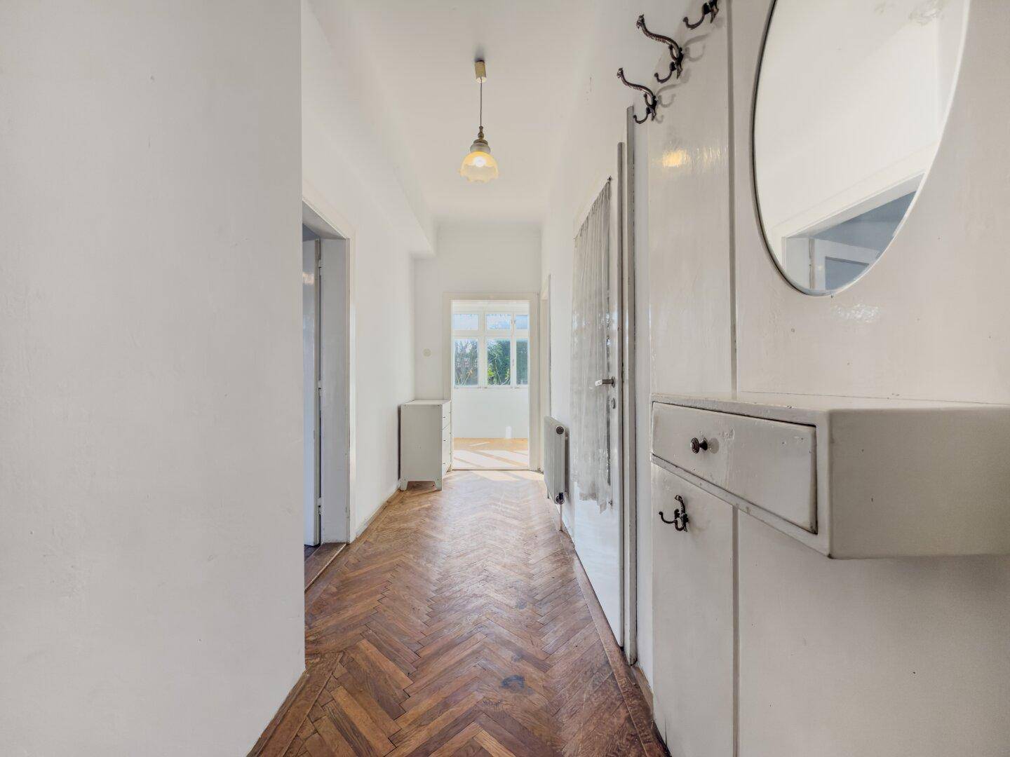 Langer Flur mit Fischgrätparkett, Spiegel und Garderobe, führt zu weiteren Räumen.