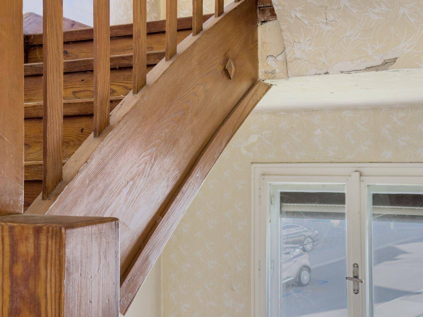 Detailansicht einer Holztreppe mit Geländer und alter Tapete im Hintergrund, zeugt von Geschichte.