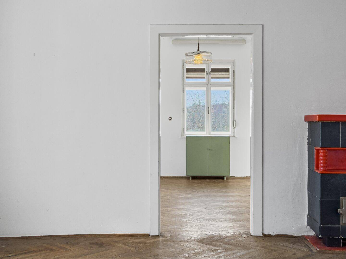 Blick durch eine Tür in einen leeren Raum mit Fenster und einem grünen Schrank.