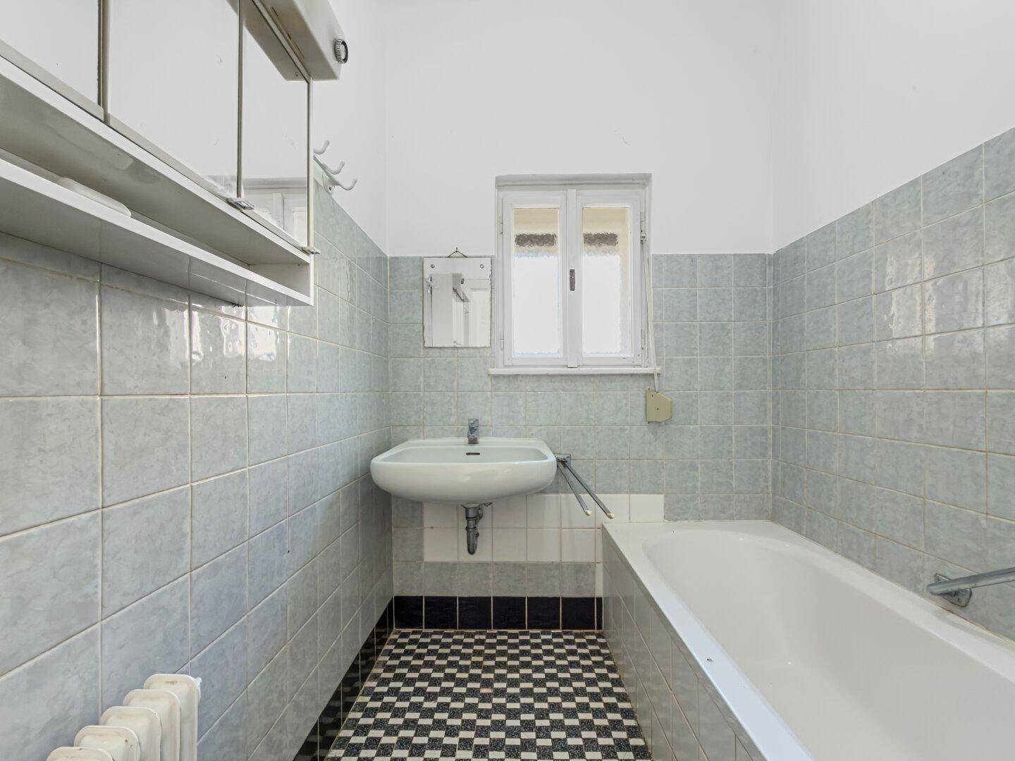 Badezimmer mit hellblauen Wandfliesen, Badewanne und Waschbecken.