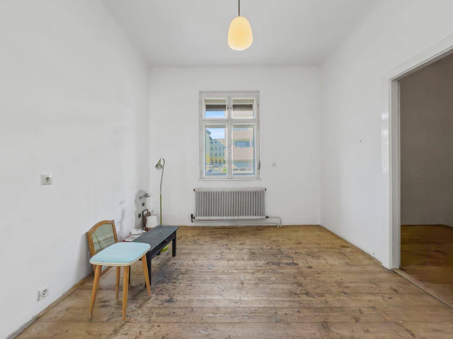 Leerer Raum mit Holzdielenboden, großem Fenster und Heizkörper.