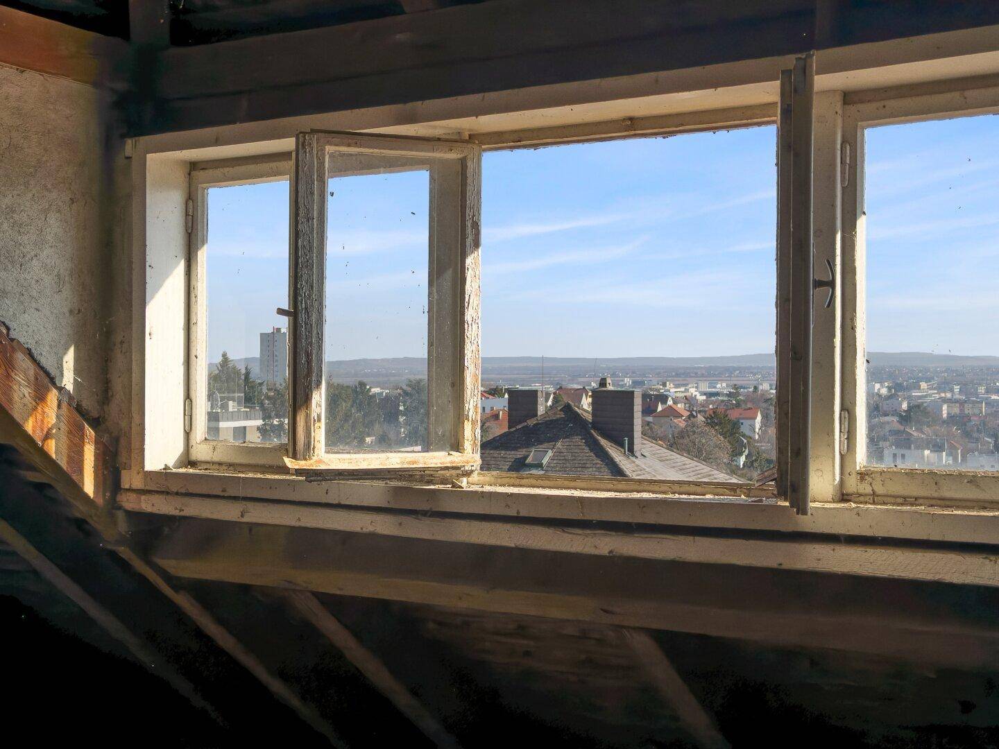 Fenster im Dachboden mit Blick über die Dächer der Stadt und die Landschaft.