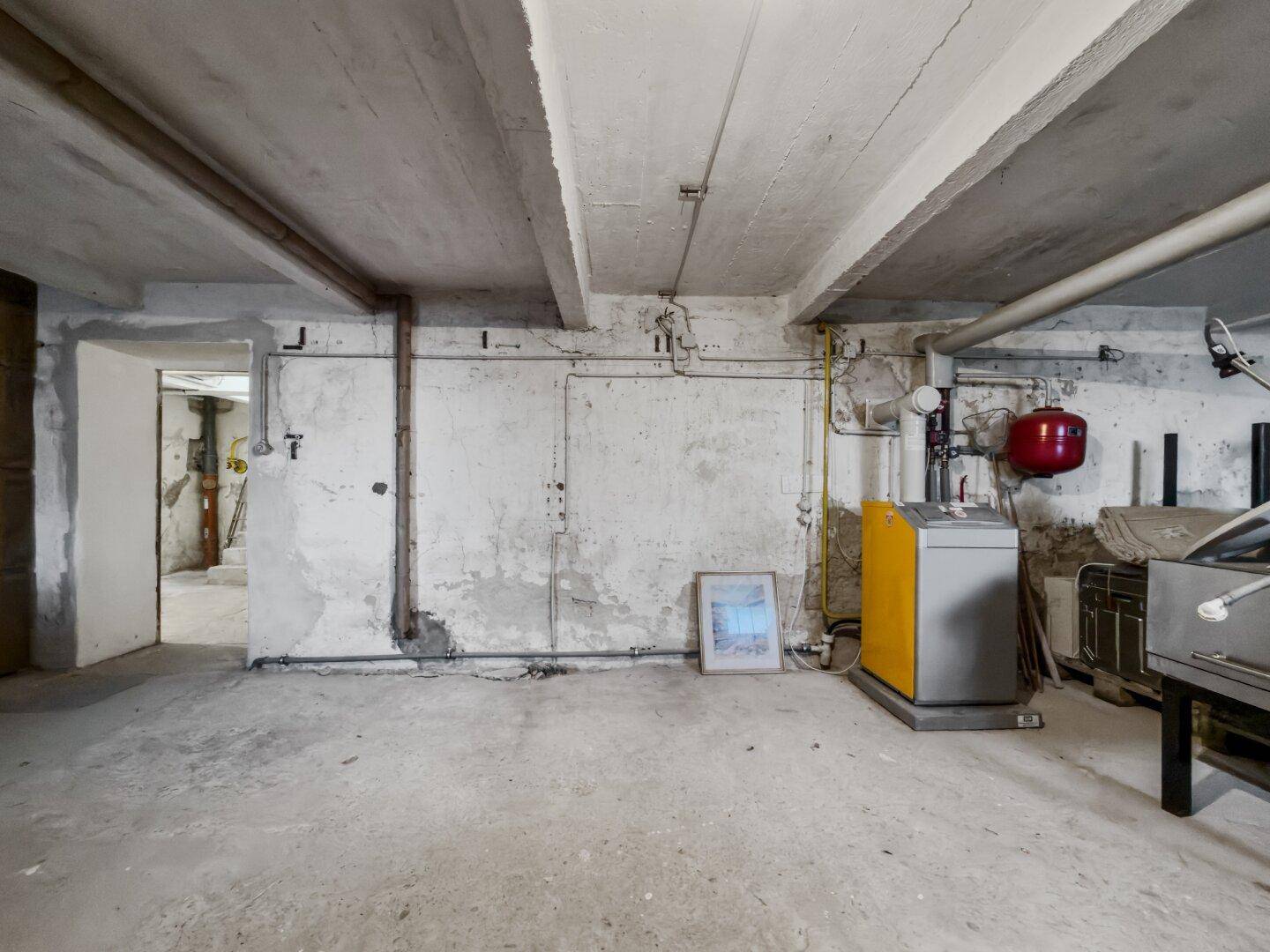 Unausgebauter Kellerraum mit Betonboden, Heizungsanlage und sichtbaren Rohren.