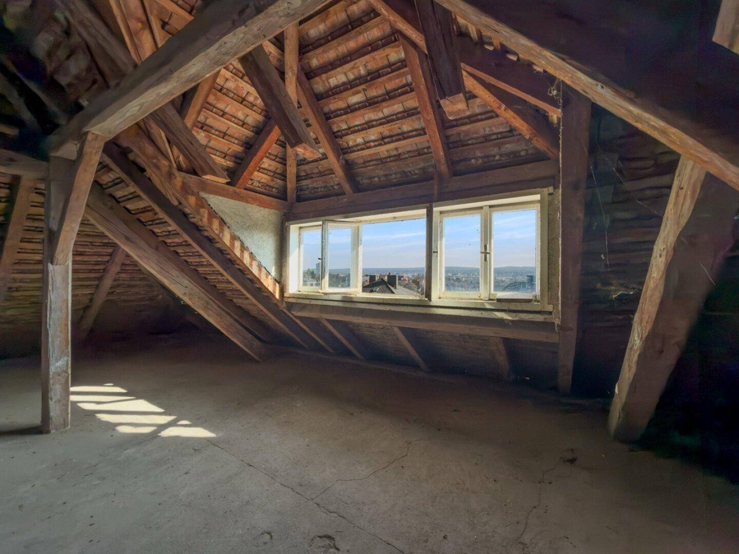Unausgebauter Dachboden mit Holzbalken, Dachschrägen und weitem Ausblick.